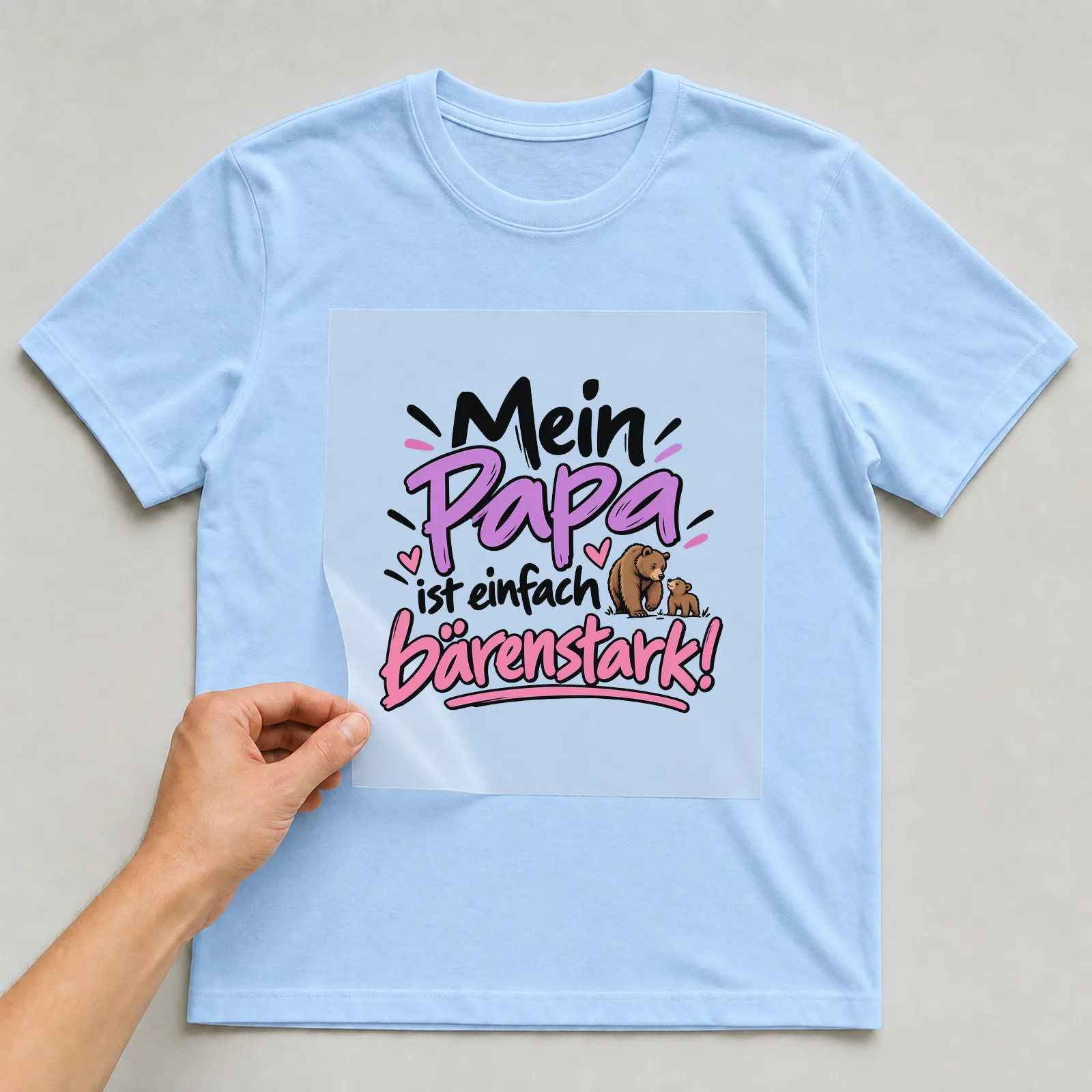 Bügelbild „Mein Papa ist einfach bärenstark!“ auf hellblauem T-Shirt, Folie wird aufgelegt