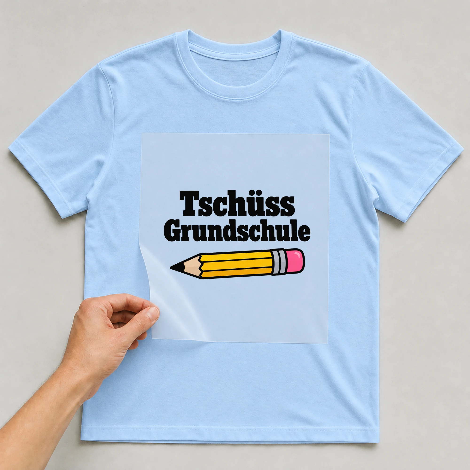 Bügelbild „Tschüss Grundschule“ auf babyblauem T-Shirt, Folie wird aufgelegt