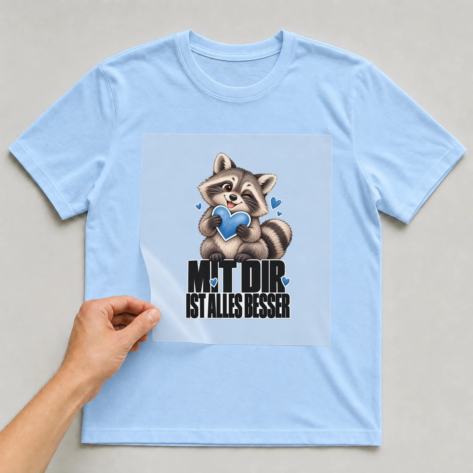 Bügelbild „Mit dir ist alles besser“ auf hellblauem T-Shirt, Folie wird aufgelegt