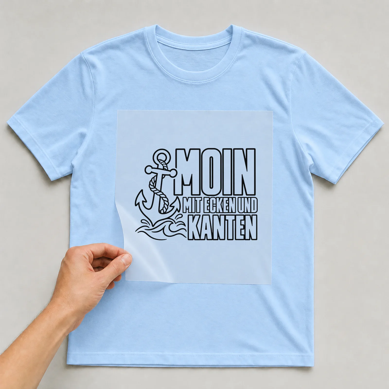 Bügelbild „Moin mit Ecken und Kanten“ auf hellblauem T-Shirt, Folie wird aufgelegt
