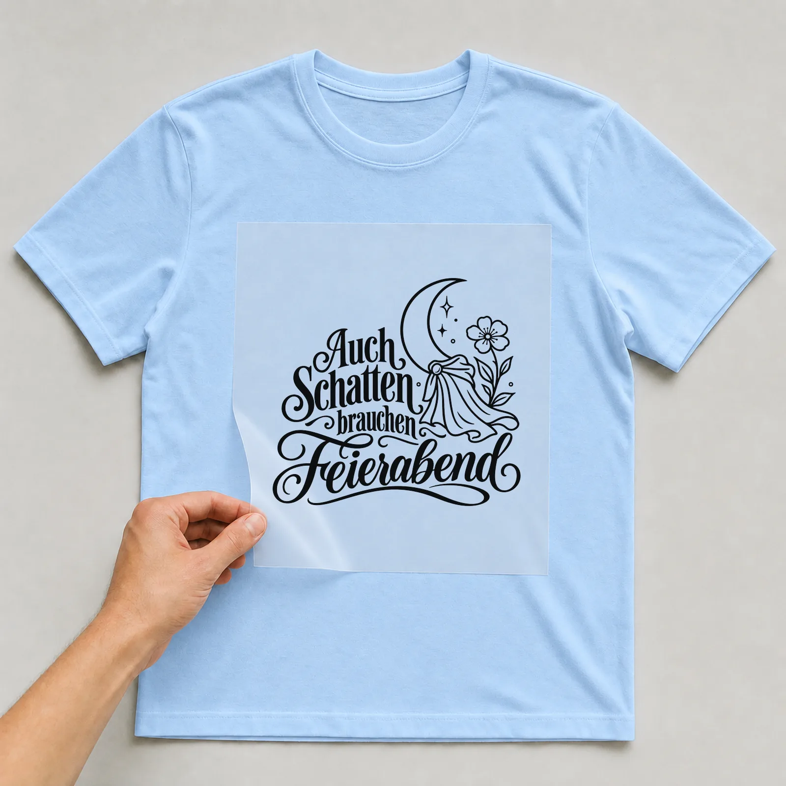 Bügelbild „Auch Schatten brauchen Feierabend“ auf hellblauem T-Shirt, Folie wird aufgelegt