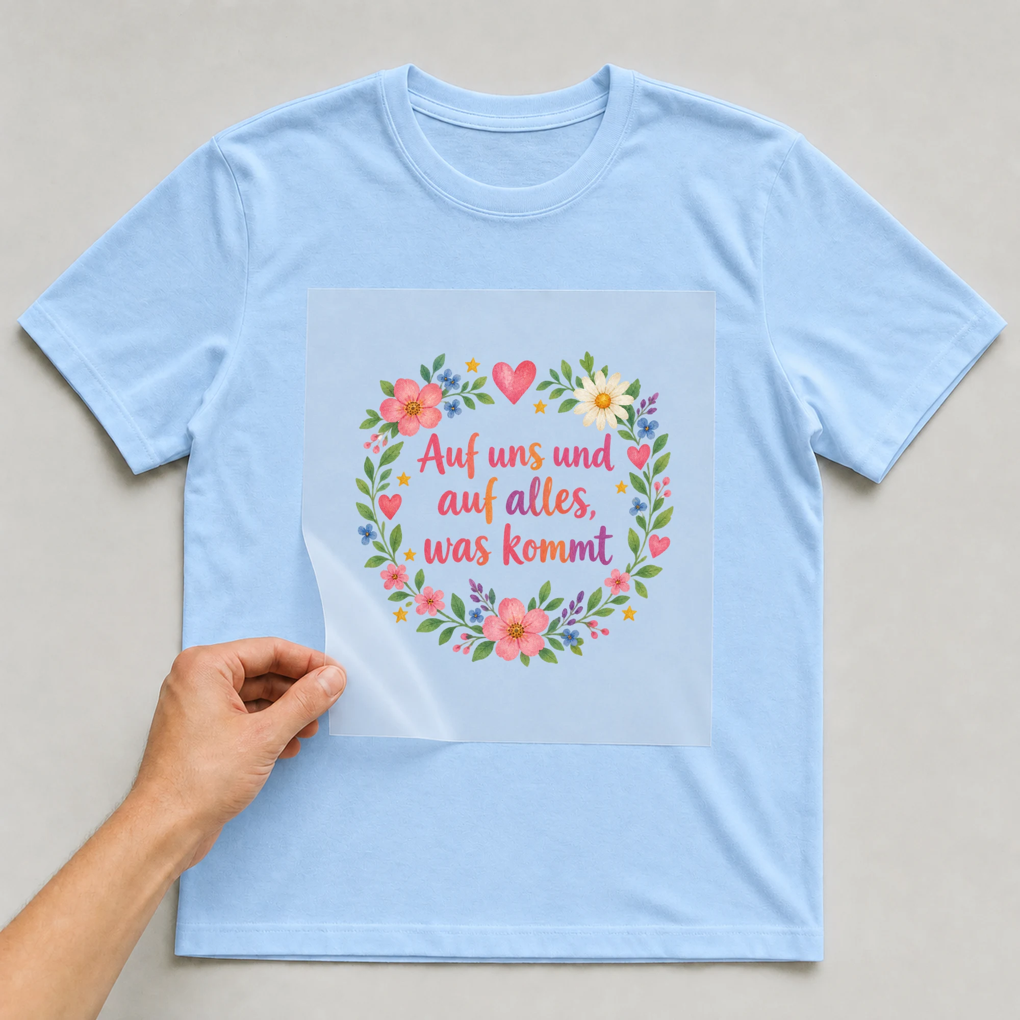 Bügelbild „Auf uns und auf alles, was kommt“ auf babyblauem T-Shirt, Folie wird aufgelegt