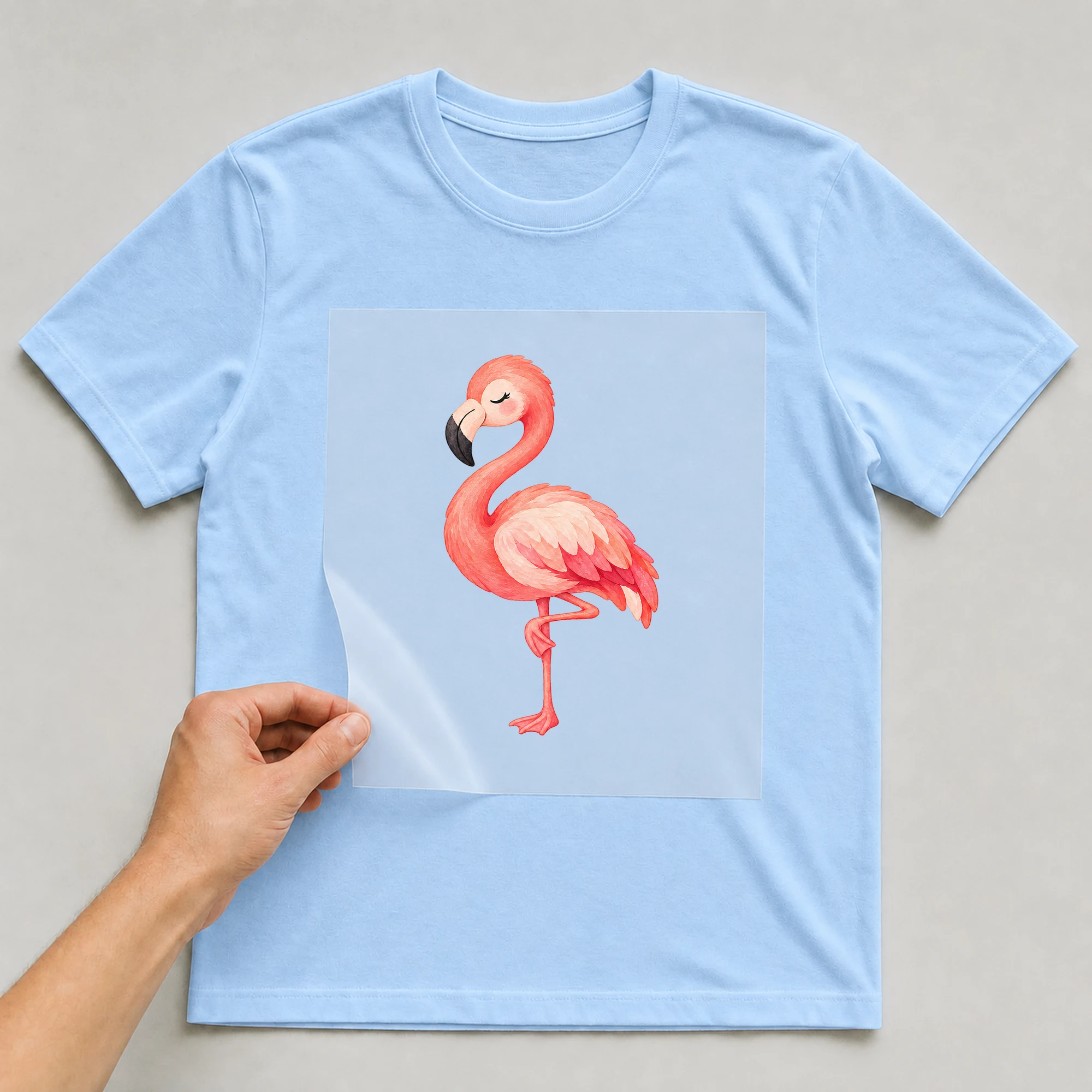 Bügelbild „Putziger Flamingo“ auf babyblauem T-Shirt, Folie wird aufgelegt