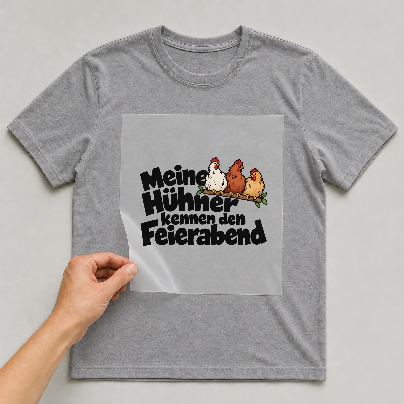 Bügelbild „Meine Hühner kennen den Feierabend“ auf grauem T-Shirt, Folie wird aufgelegt