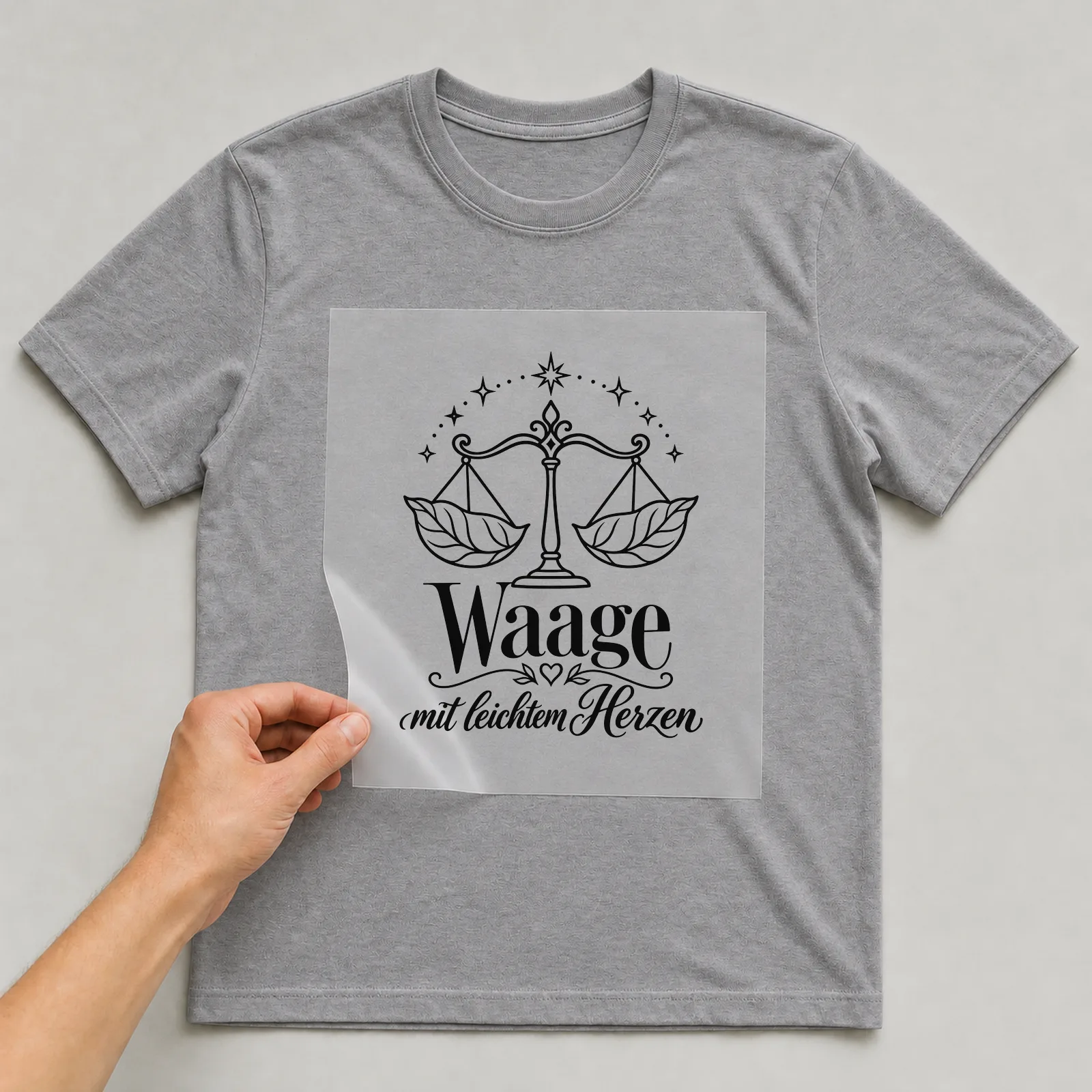 Bügelbild „Waage mit leichtem Herzen“ auf grauem T-Shirt, Folie wird aufgelegt