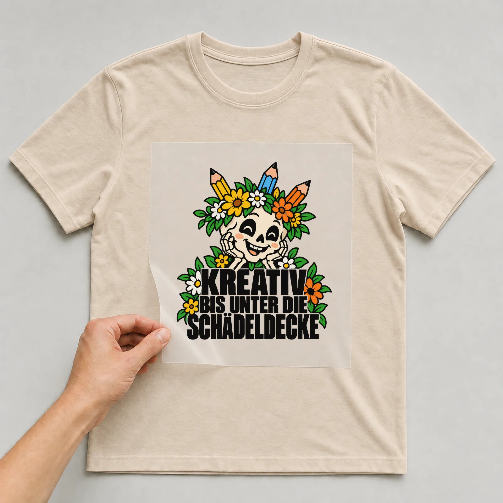 Bügelbild „Kreativ bis unter die Schädeldecke“ auf beigem T-Shirt, Folie wird aufgelegt