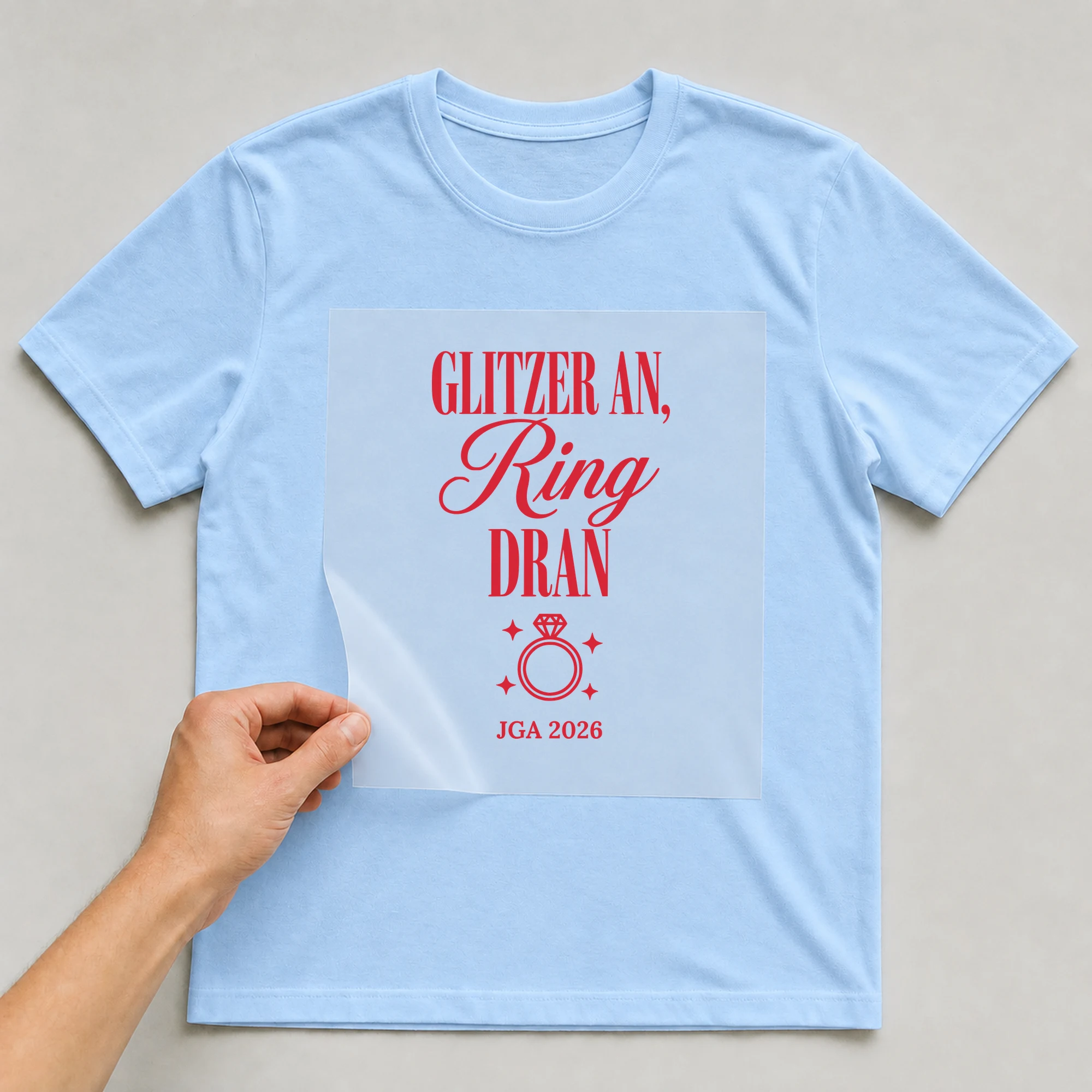 Bügelbild Glitzer an, Ring dran auf hellblauem T-Shirt, Folie wird aufgelegt