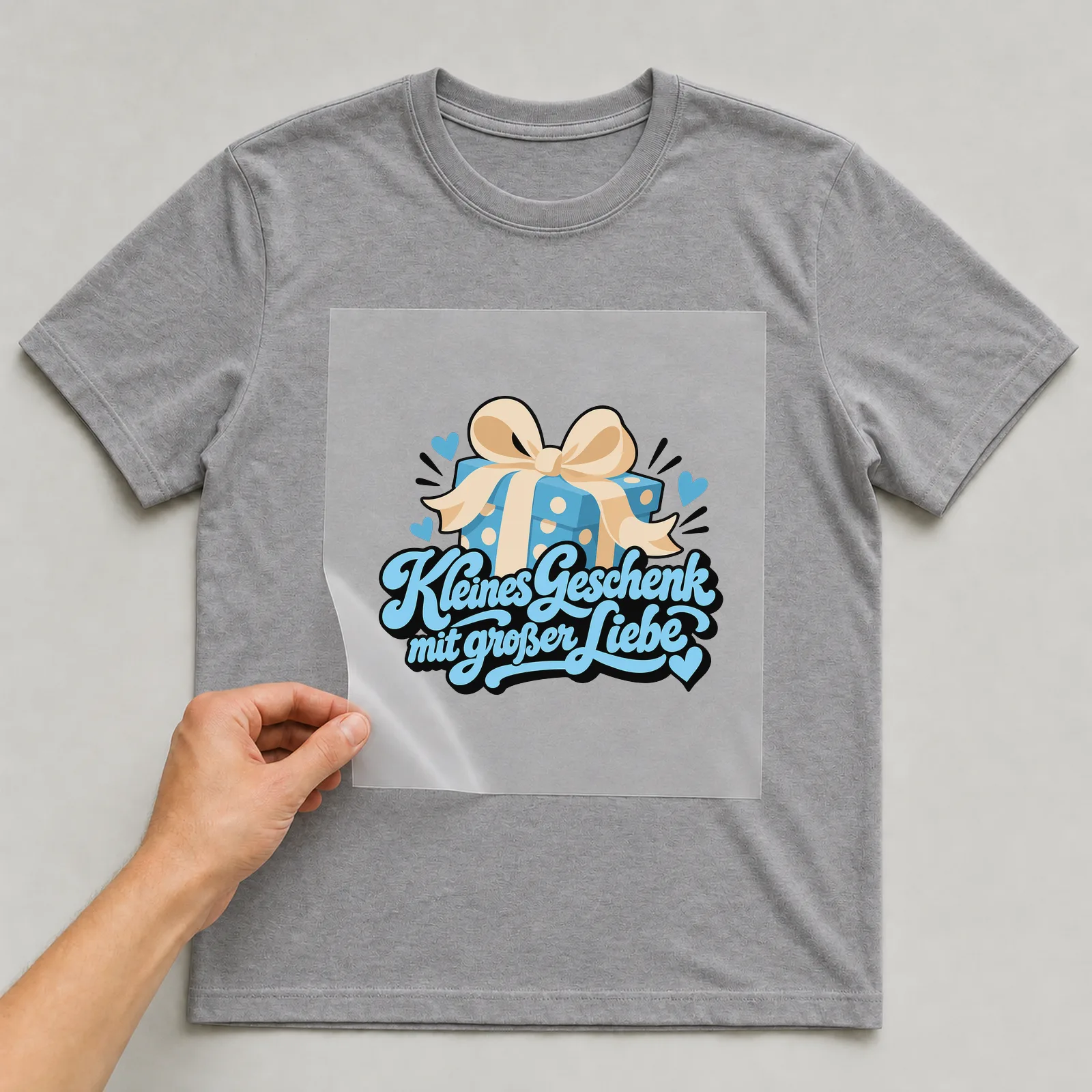Bügelbild „Kleines Geschenk mit großer Liebe“ auf grauem T-Shirt, Folie wird aufgelegt