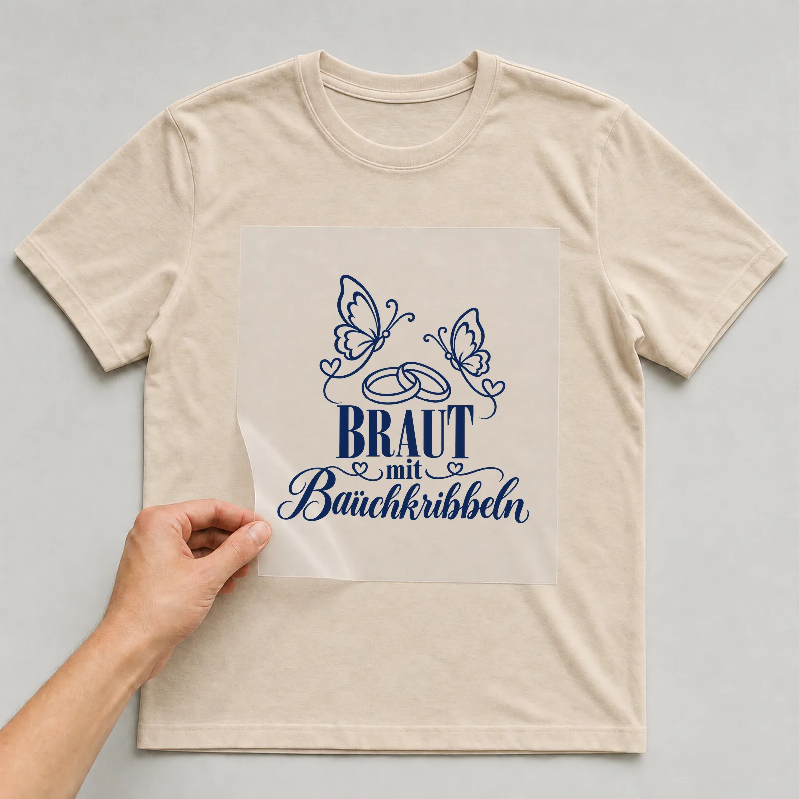 Bügelbild „Braut mit Bauchkribbeln“ auf beigem T-Shirt, Folie wird aufgelegt