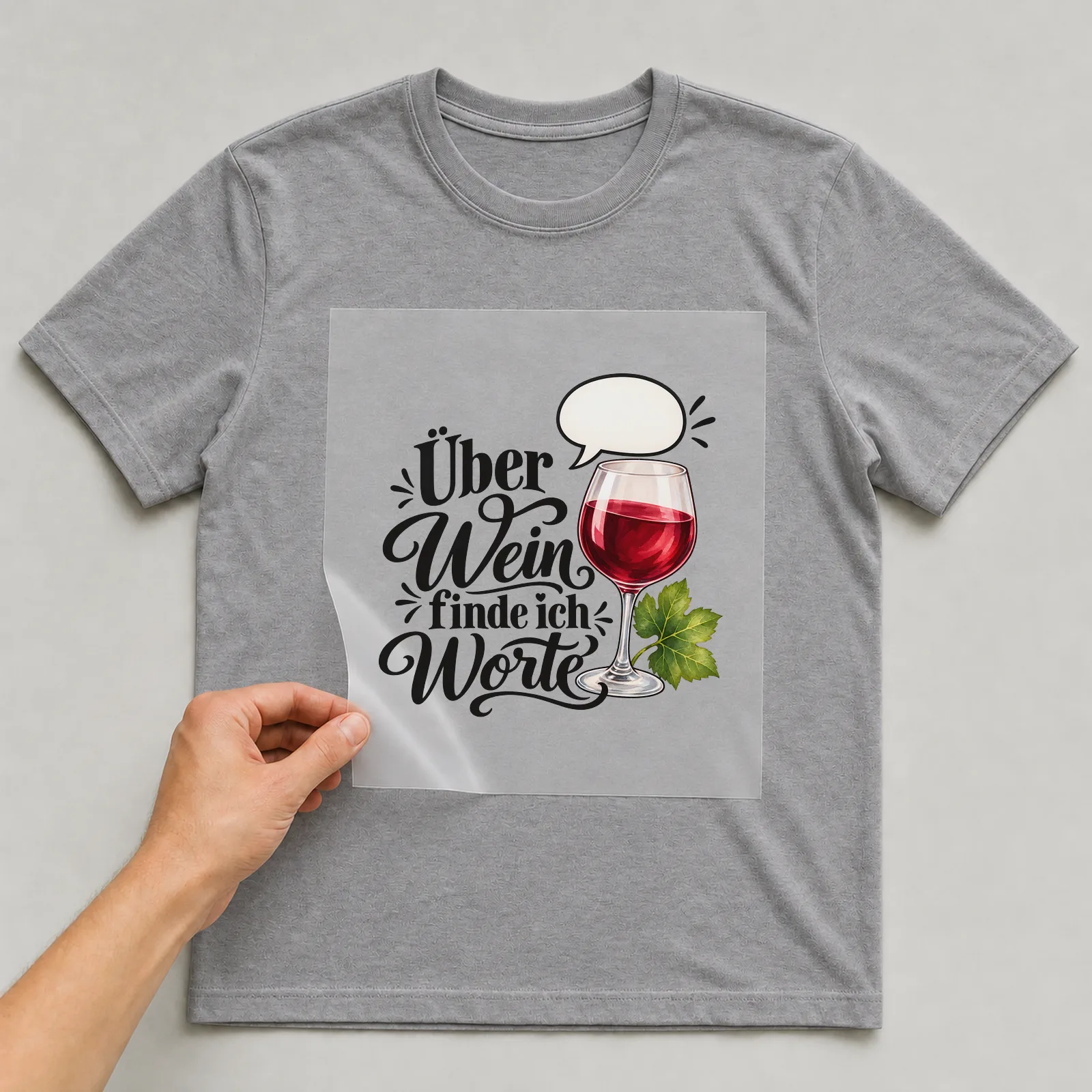 Bügelbild „Über Wein finde ich Worte“ auf grauem T-Shirt, Folie wird aufgelegt