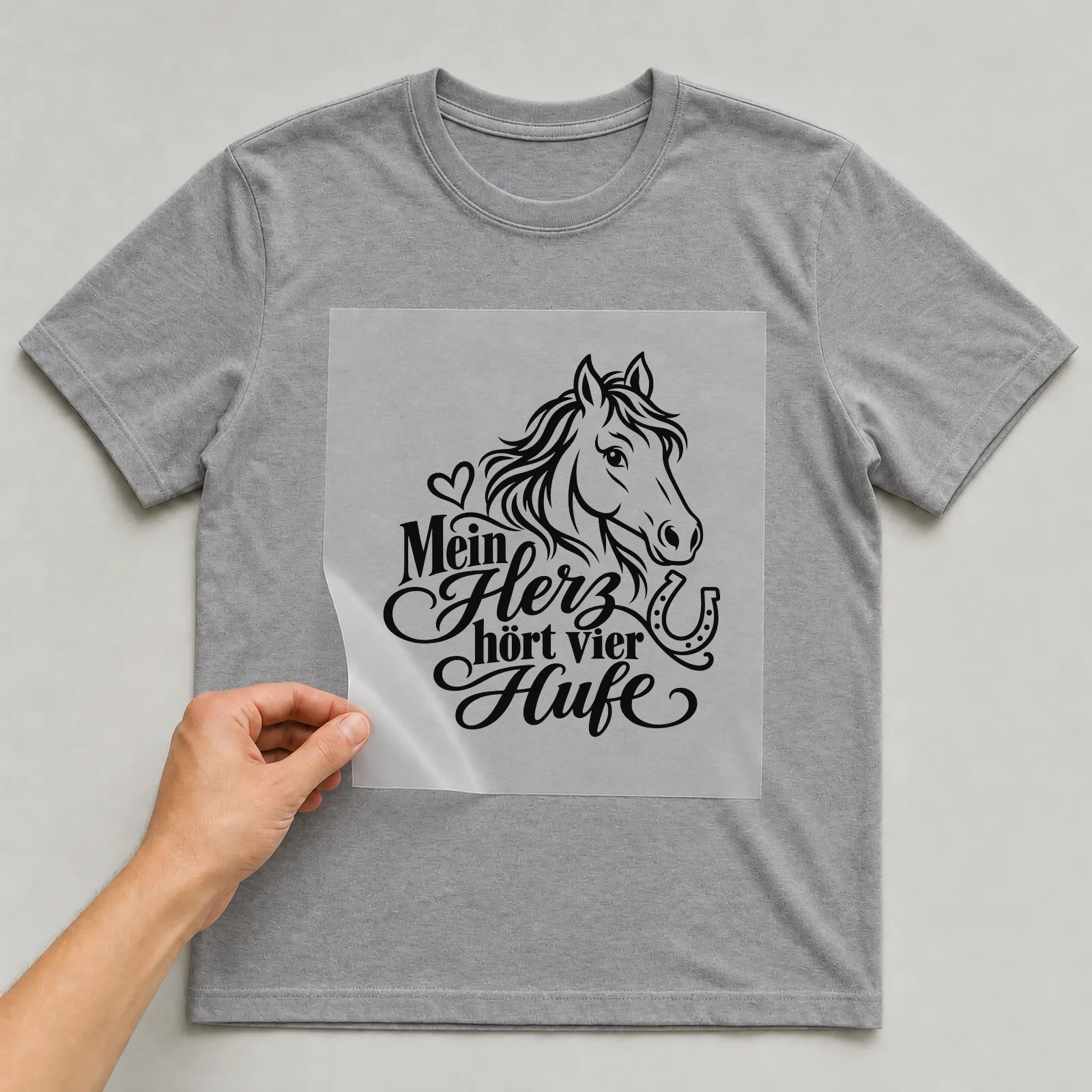 Bügelbild „Mein Herz hört vier Hufe“ auf grauem T-Shirt, Folie wird aufgelegt