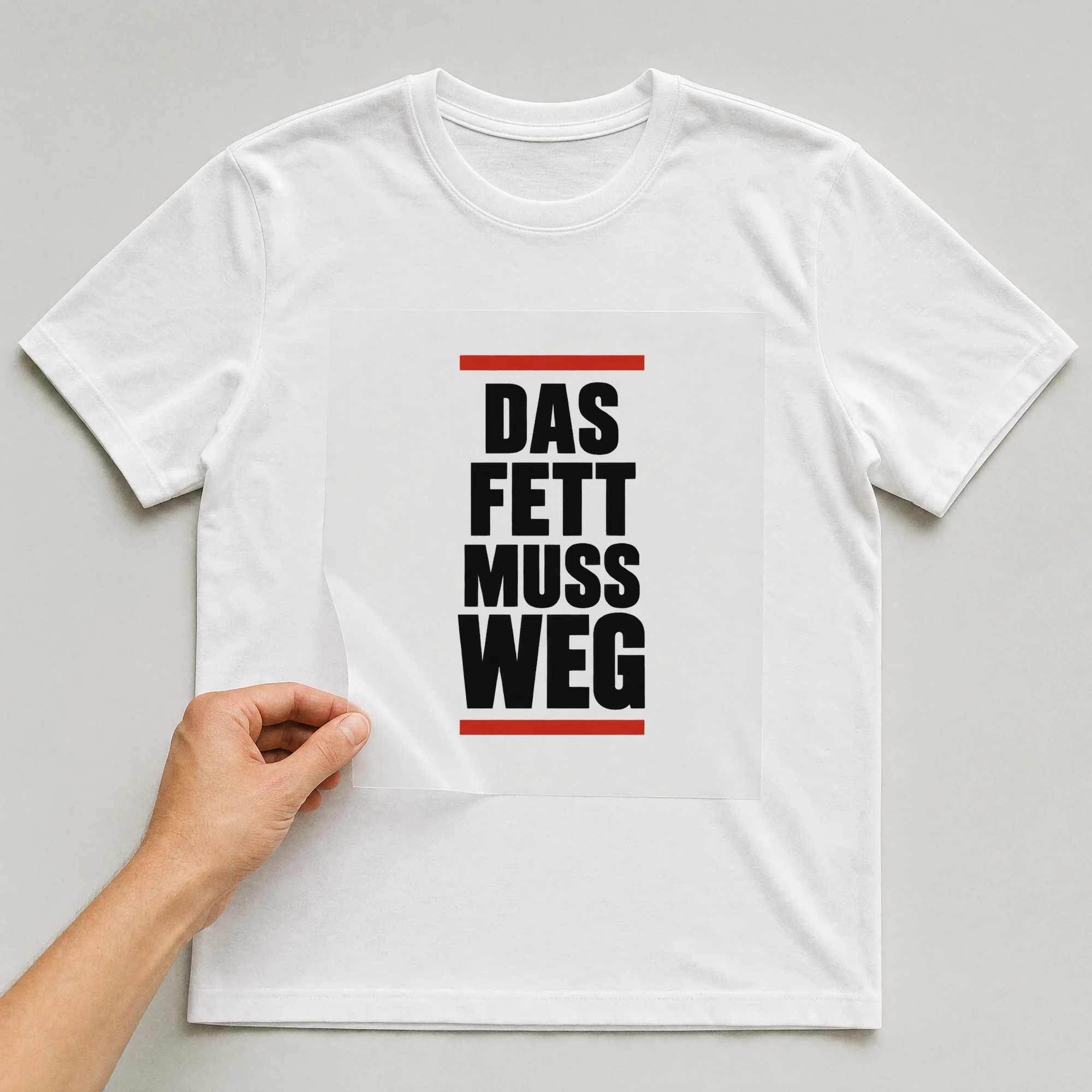 Bügelbild „Das Fett muss weg“ auf weißem T-Shirt, Folie wird aufgelegt