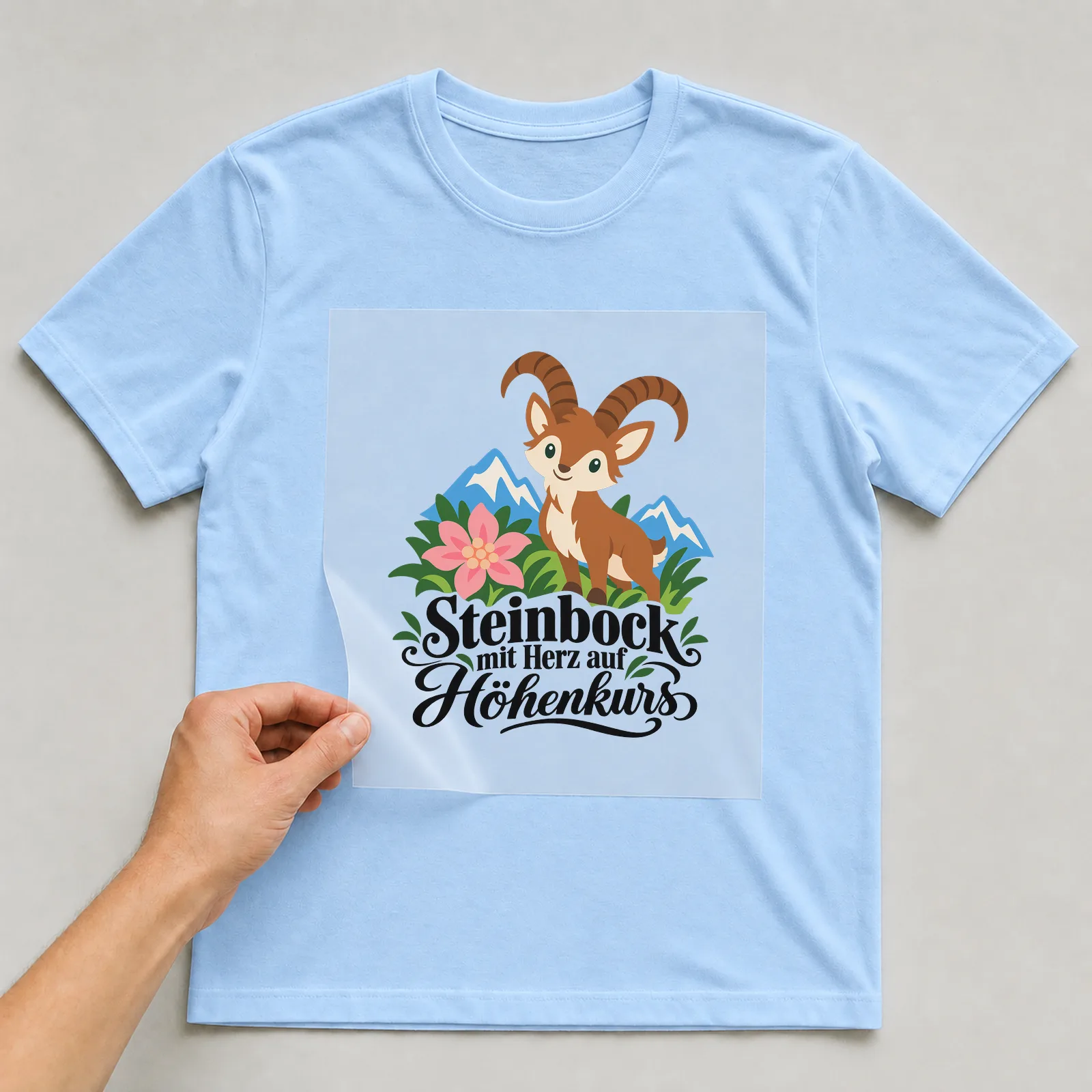 Bügelbild „Steinbock mit Herz auf Höhenkurs“ auf hellblauem T-Shirt, Folie wird aufgelegt