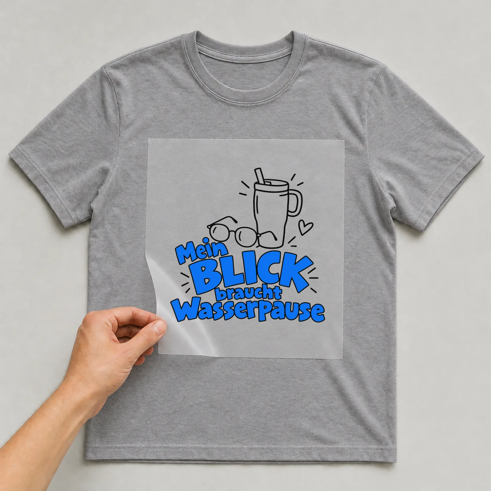 Bügelbild „Mein Blick braucht Wasserpause“ auf grauem T-Shirt, Folie wird aufgelegt