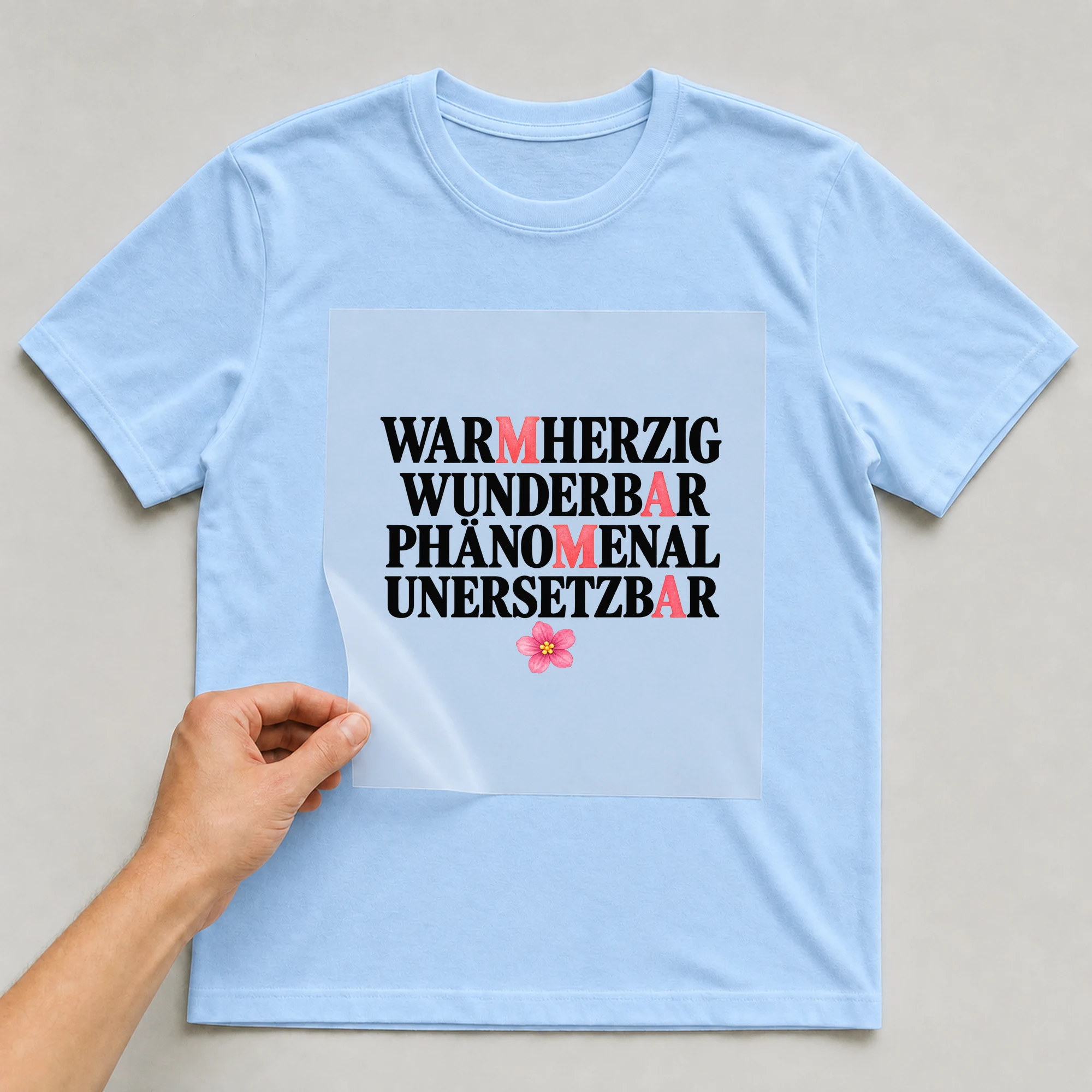 Bügelbild „Warmherzig Wunderbar Phänomenal Unersetzbar“ auf babyblauem T-Shirt, Folie wird aufgelegt
