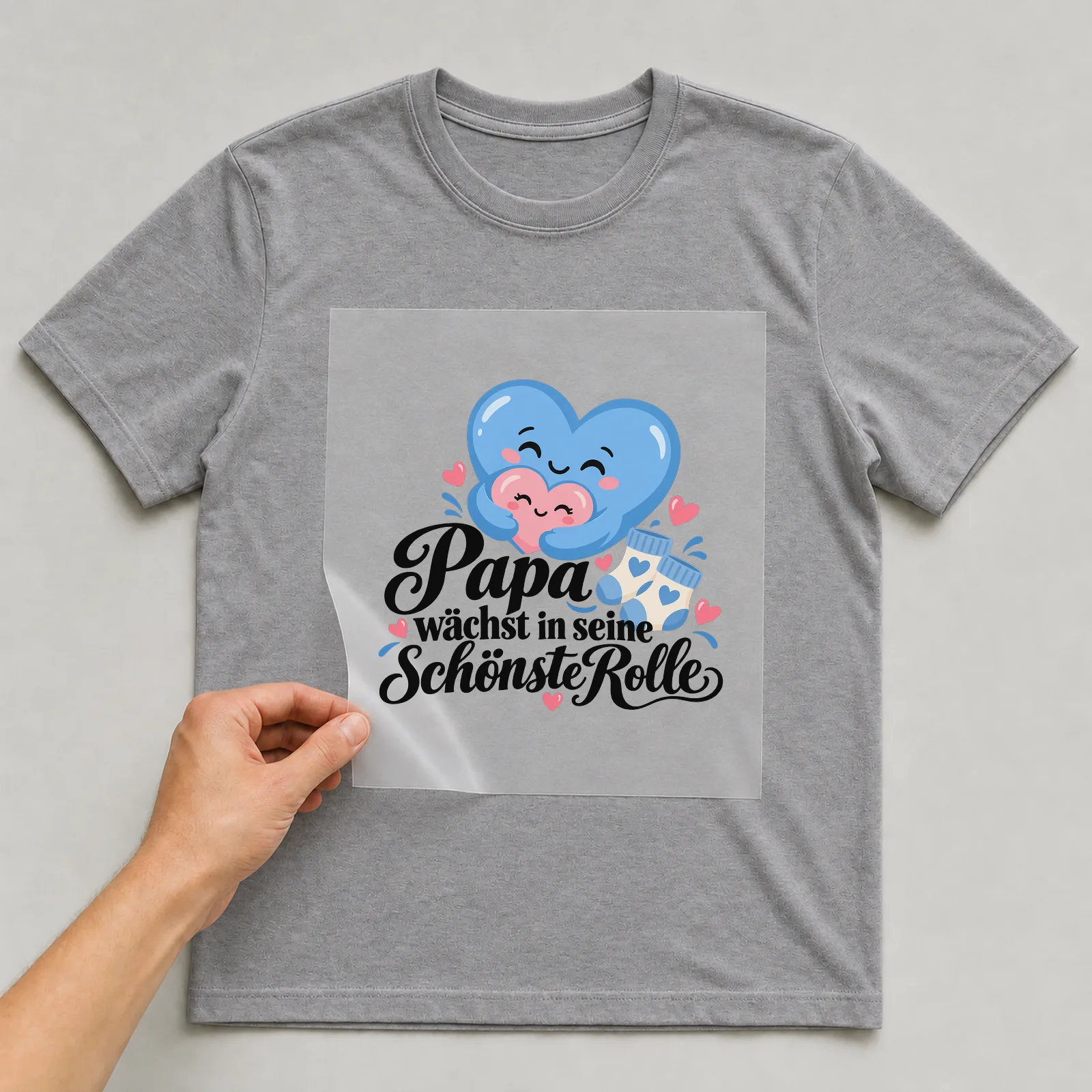 Bügelbild „Papa wächst in seine schönste Rolle“ auf grauem T-Shirt, Folie wird aufgelegt