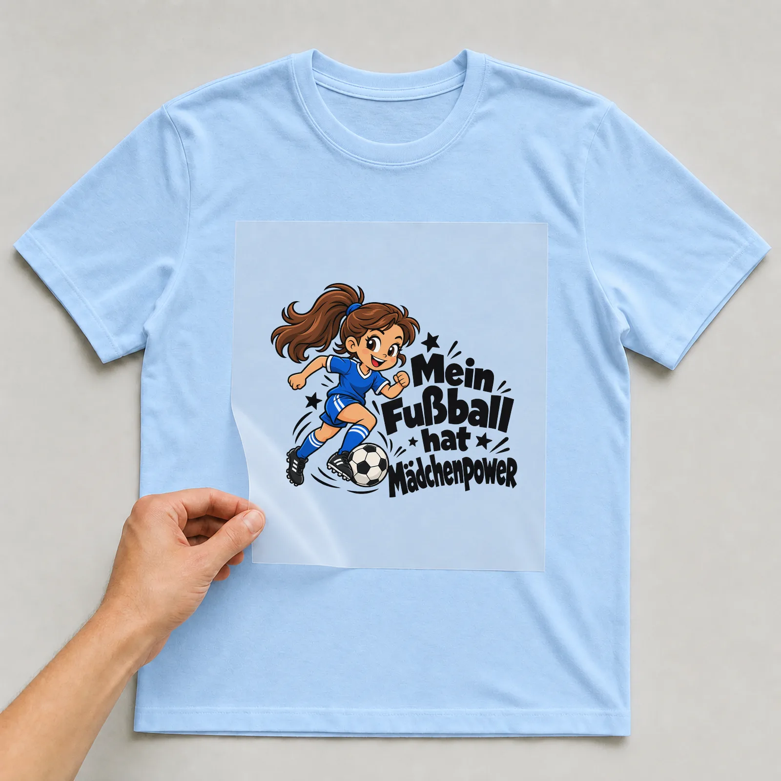 Bügelbild „Mein Fußball hat Mädchenpower“ auf hellblauem T-Shirt, Folie wird aufgelegt