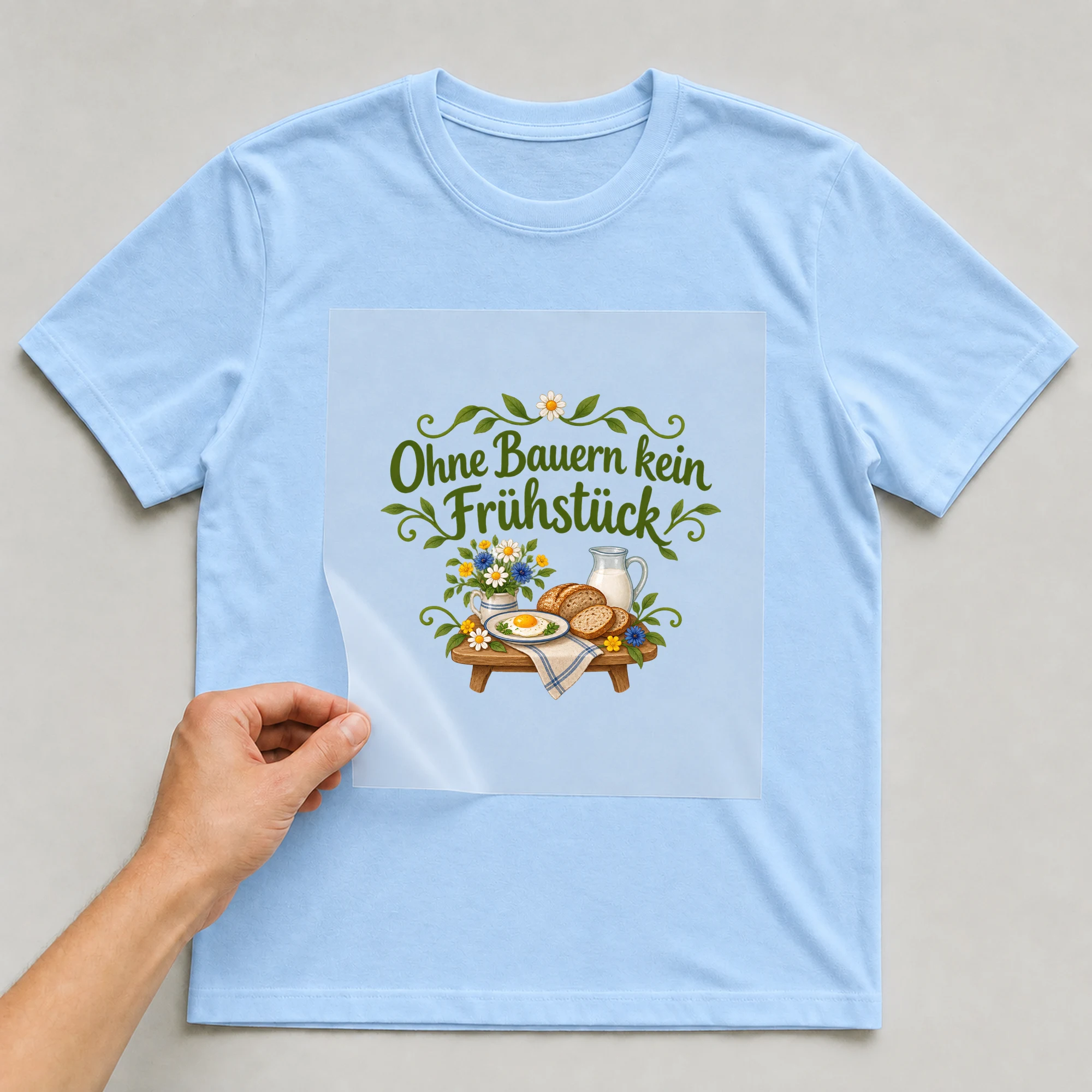 Bügelbild „Ohne Bauern kein Frühstück“ auf babyblauem T-Shirt, Folie wird aufgelegt