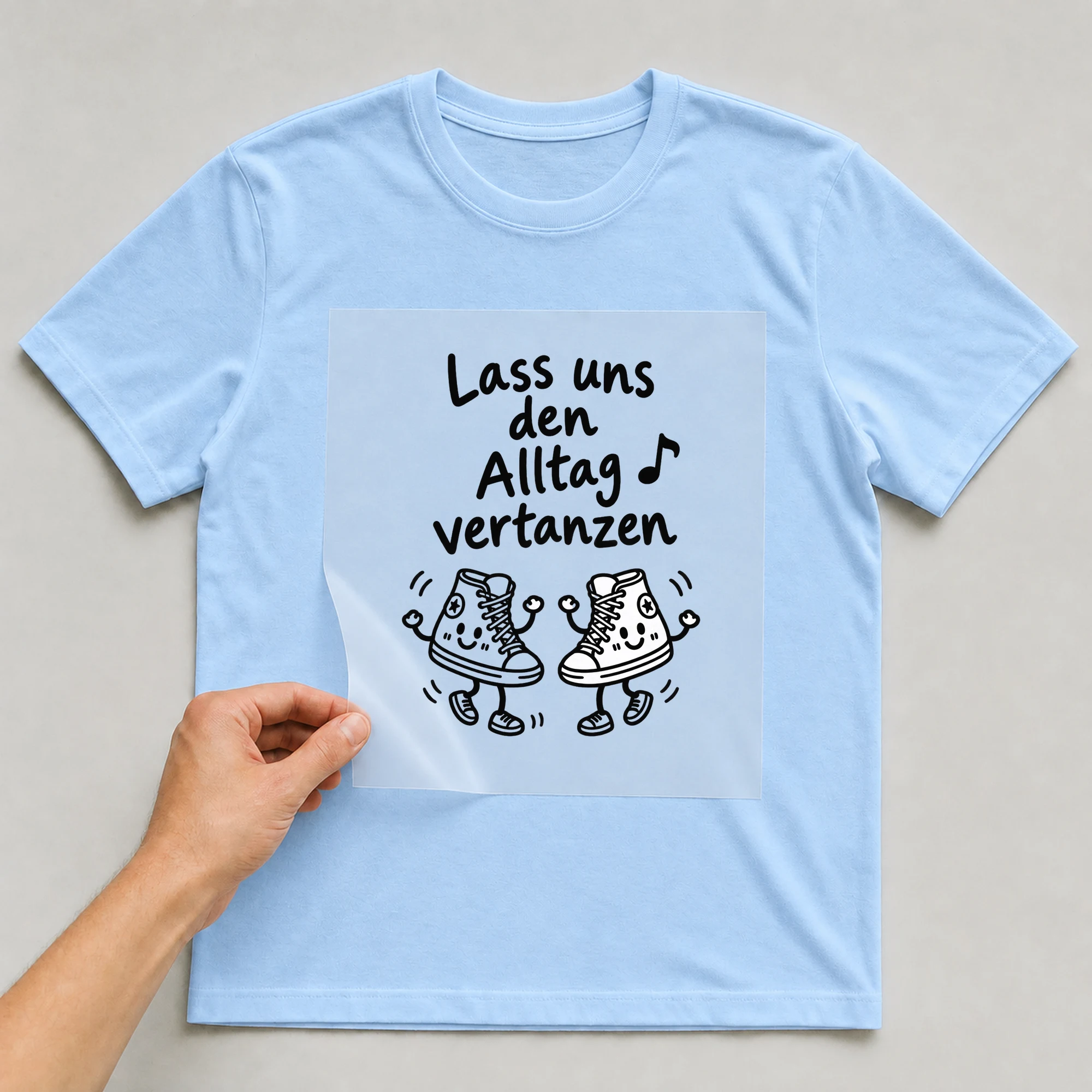 Bügelbild „Lass uns den Alltag vertanzen“ auf babyblauem T-Shirt, Folie wird aufgelegt