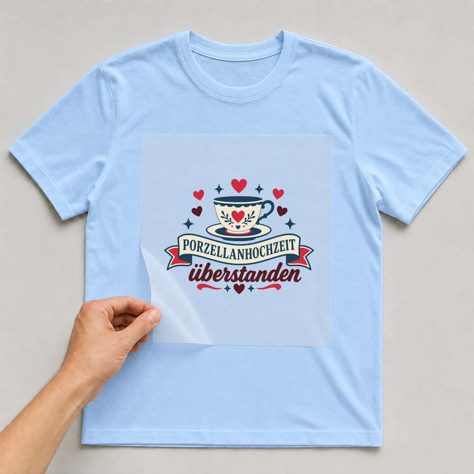 Bügelbild Porzellanhochzeit überstanden auf hellblauem T-Shirt, Folie wird aufgelegt