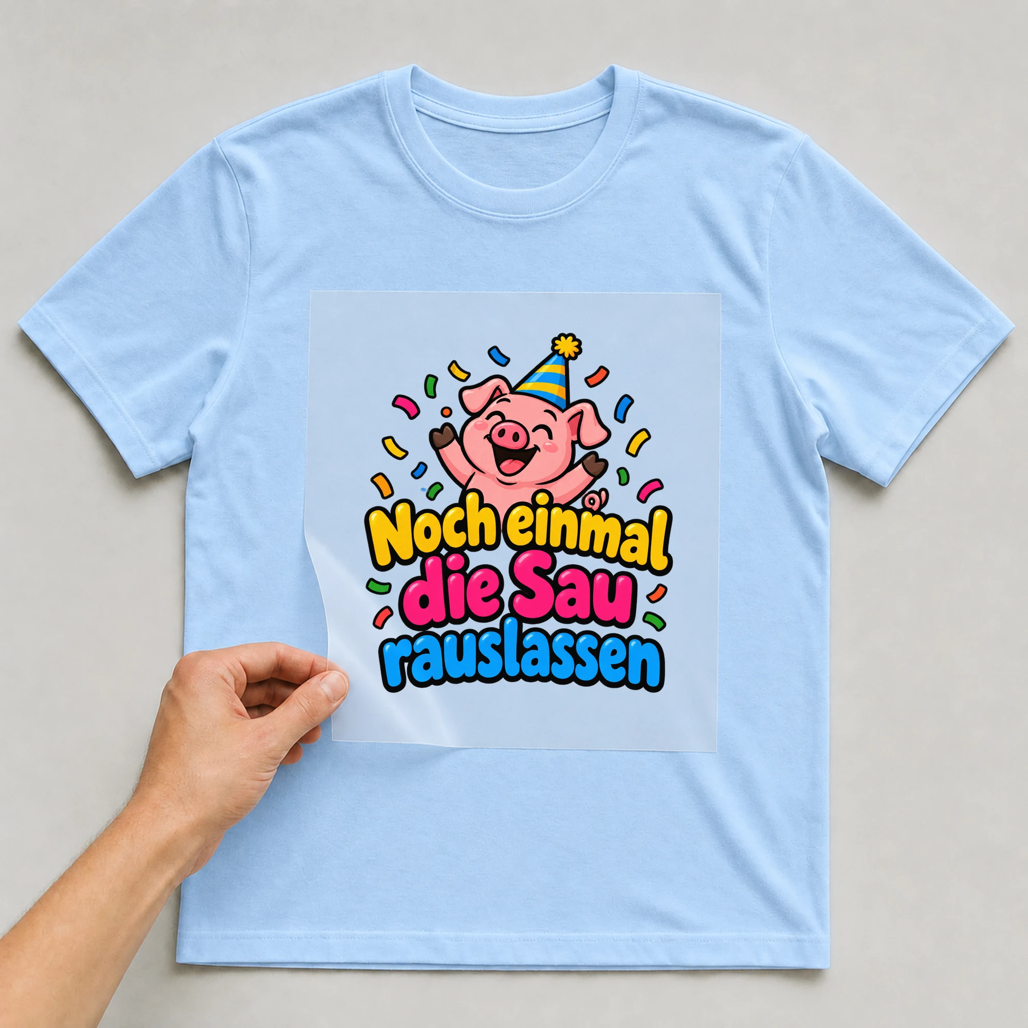 Bügelbild „Noch einmal die sau rauslassen“ auf babyblauem T-Shirt, Folie wird aufgelegt