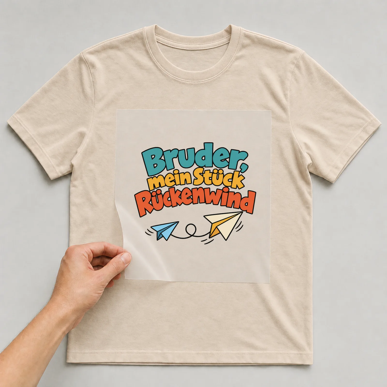 Bügelbild „Bruder, mein Stück Rückenwind“ auf beigem T-Shirt, Folie wird aufgelegt