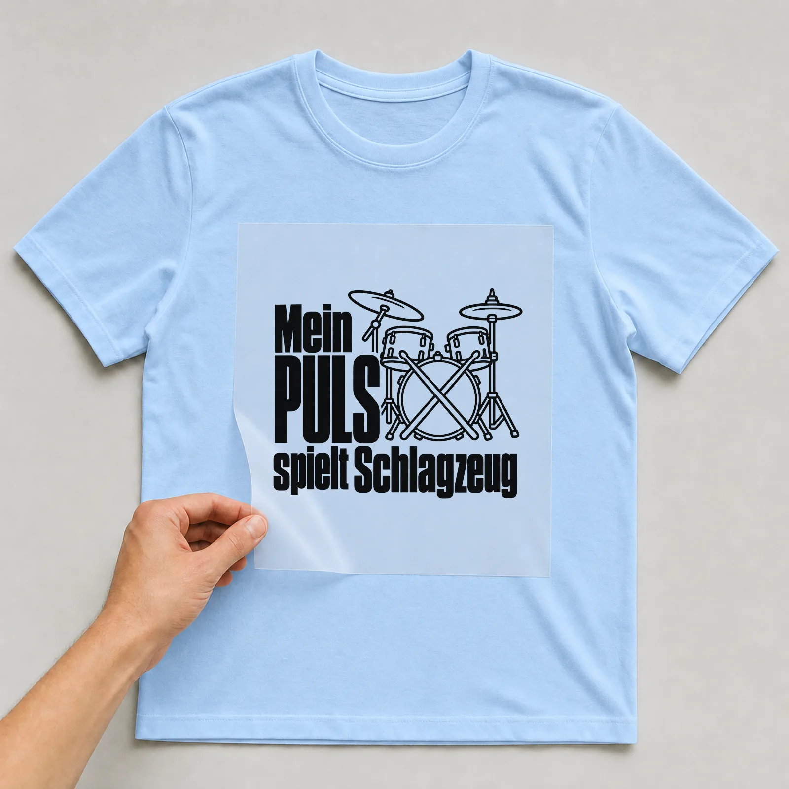 Bügelbild „Mein Puls spielt Schlagzeug“ auf hellblauem T-Shirt, Folie wird aufgelegt