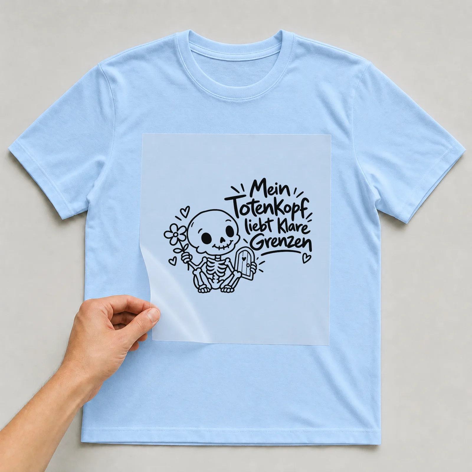 Bügelbild „Mein Totenkopf liebt klare Grenzen“ auf hellblauem T-Shirt, Folie wird aufgelegt