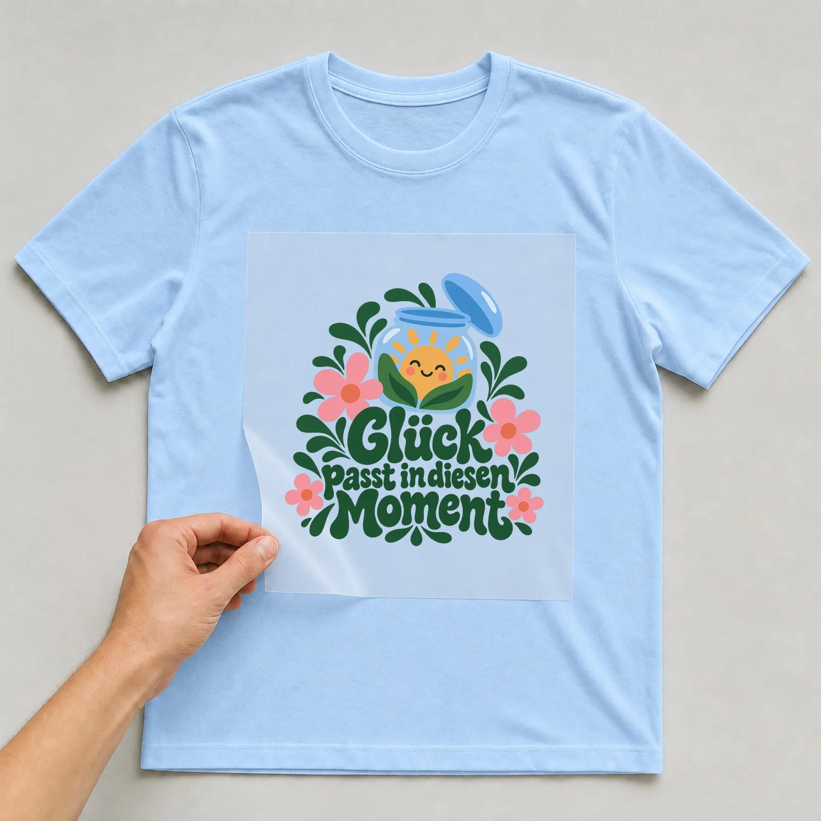 Bügelbild „Glück passt in diesen Moment“ auf hellblauem T-Shirt, Folie wird aufgelegt