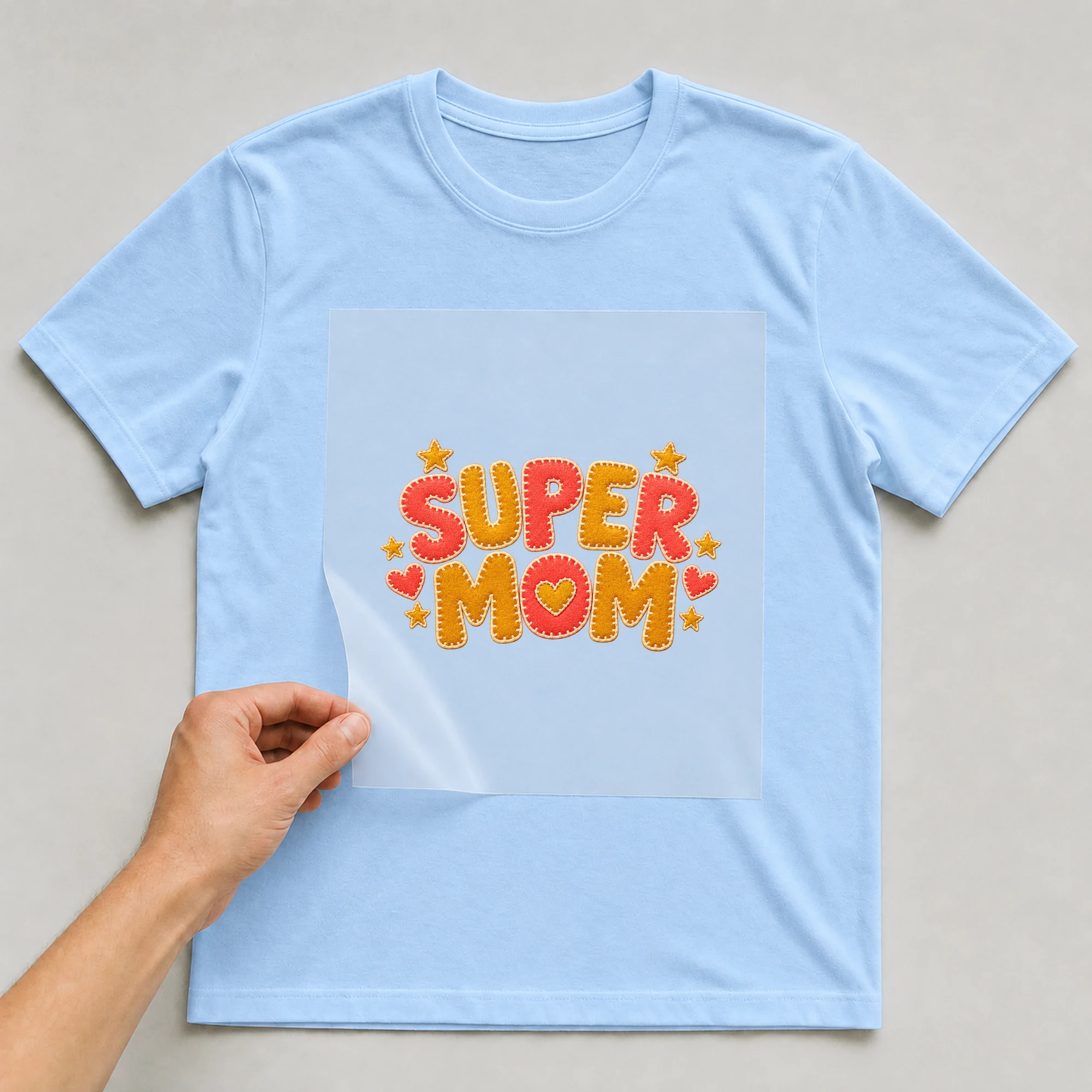 Bügelbild „Super Mom“ auf babyblauem T-Shirt, Folie wird aufgelegt