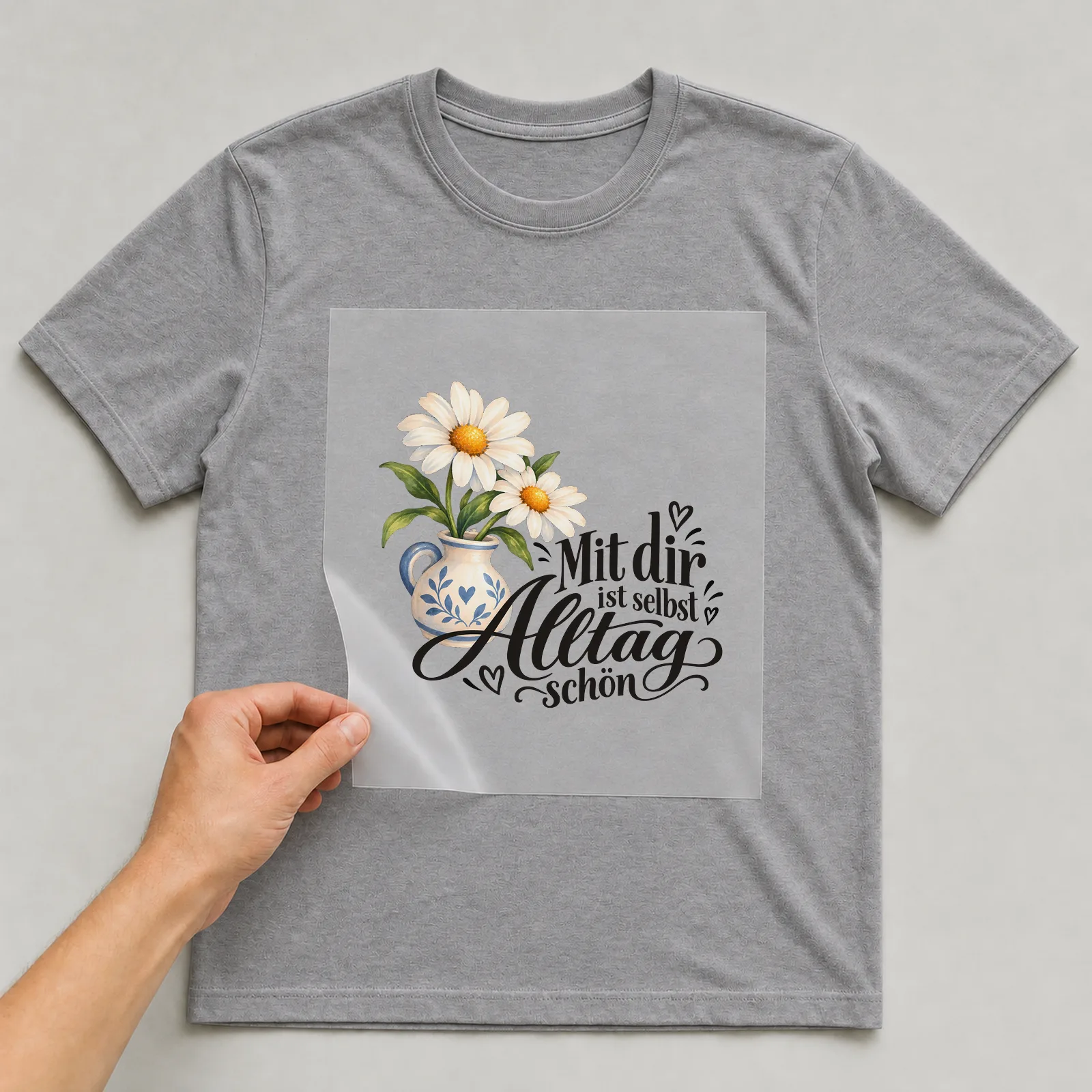 Bügelbild „Mit dir ist selbst Alltag schön“ auf grauem T-Shirt, Folie wird aufgelegt