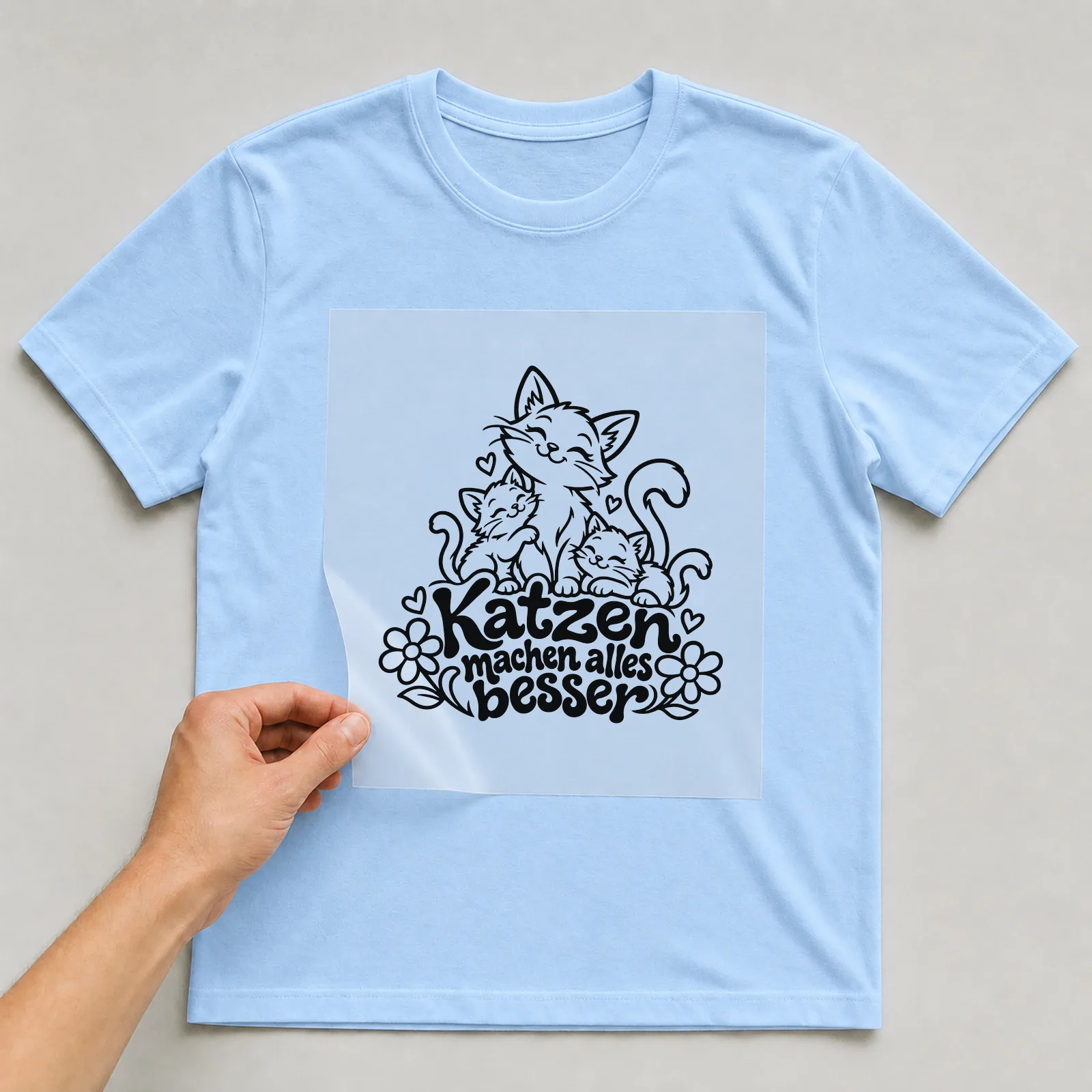 Bügelbild „Katzen machen alles besser“ (klaren Konturen) auf hellblauem T-Shirt, Folie wird aufgelegt