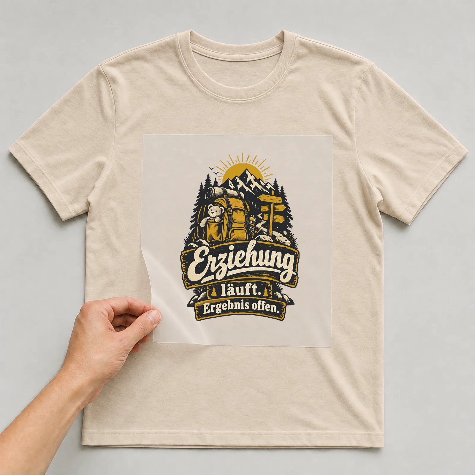Bügelbild Erziehung läuft. Ergebnis offen. auf beigem T-Shirt, Folie wird aufgelegt