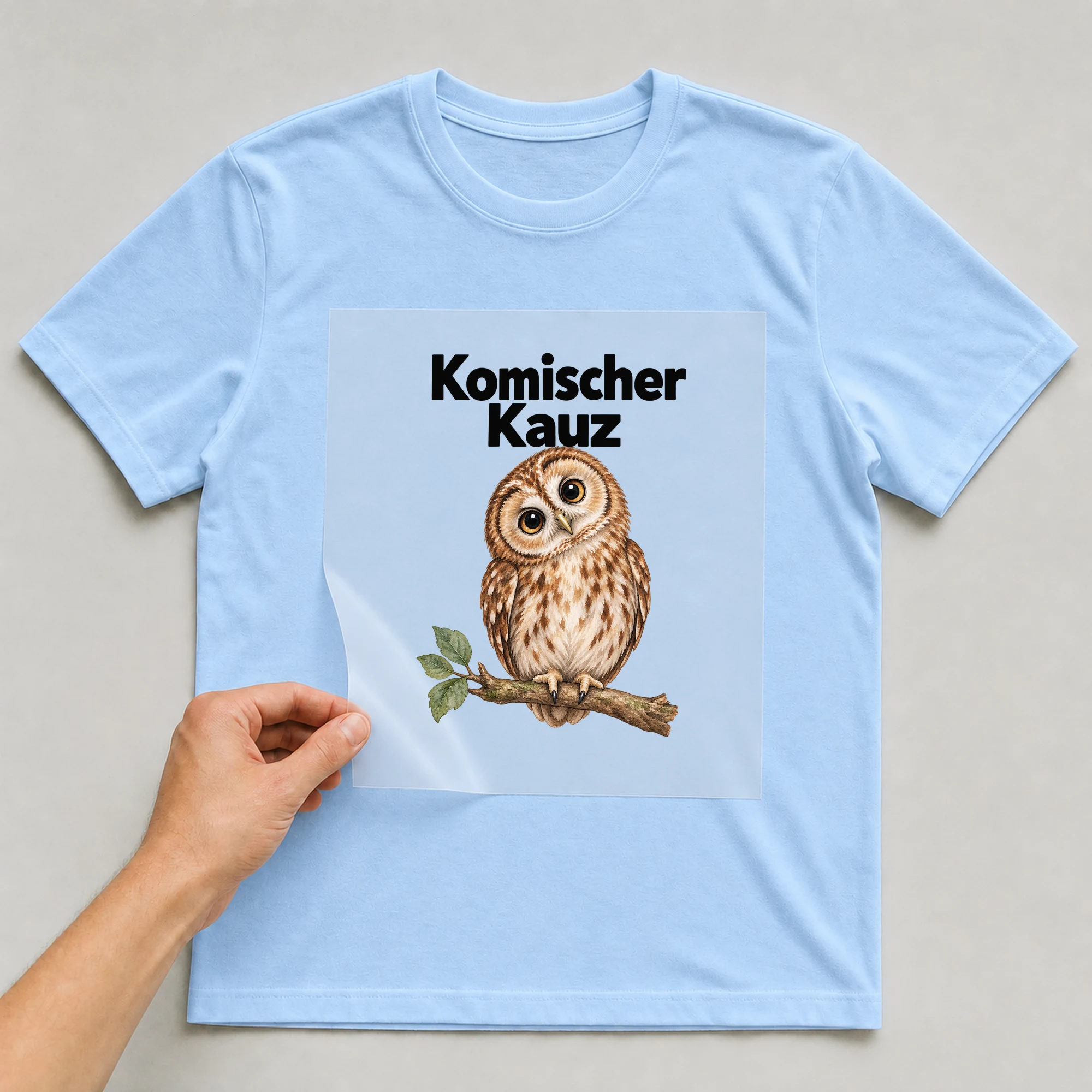 Bügelbild „Komischer Kauz“ auf babyblauem T-Shirt, Folie wird aufgelegt