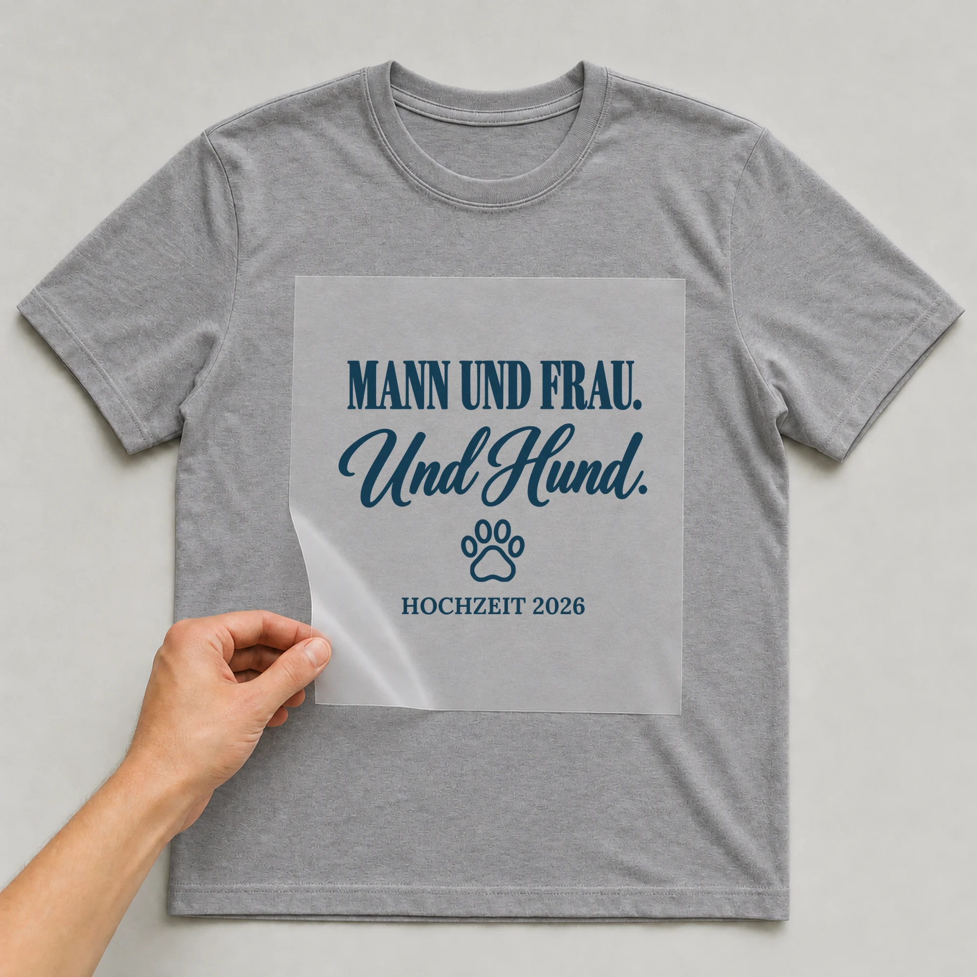 Bügelbild Mann und Frau. Und Hund mit Jahr auf grauem T-Shirt, Folie wird aufgelegt