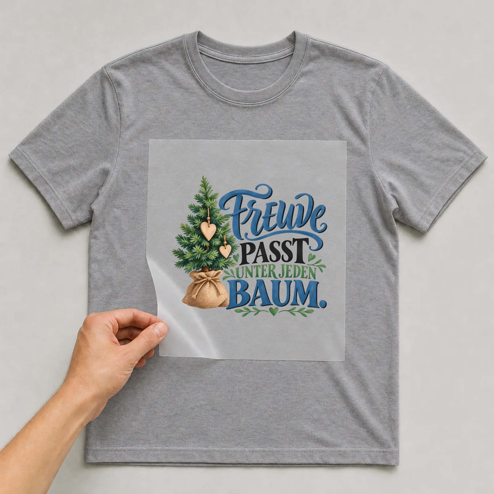 Bügelbild „Freude passt unter jeden Baum“ auf grauem T-Shirt, Folie wird aufgelegt