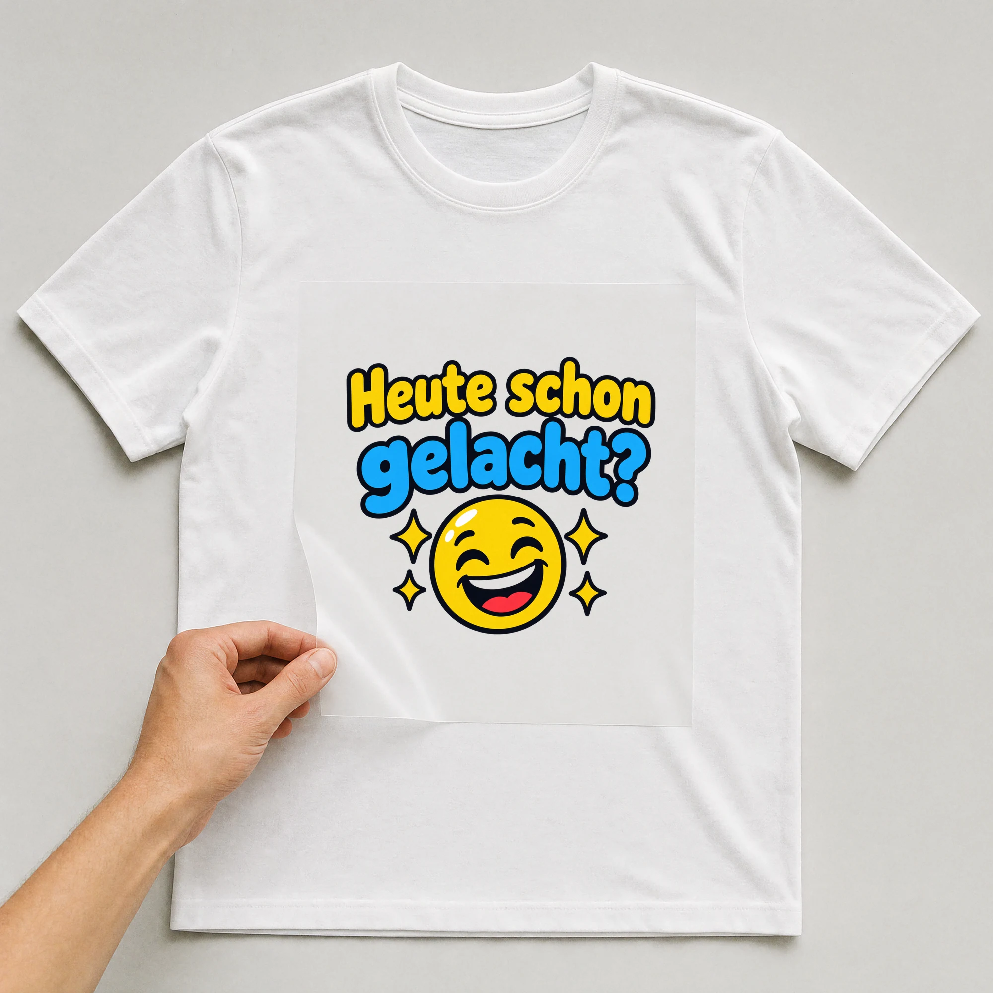Bügelbild „Heute schon gelacht?“ auf weißem T-Shirt, Folie wird aufgelegt