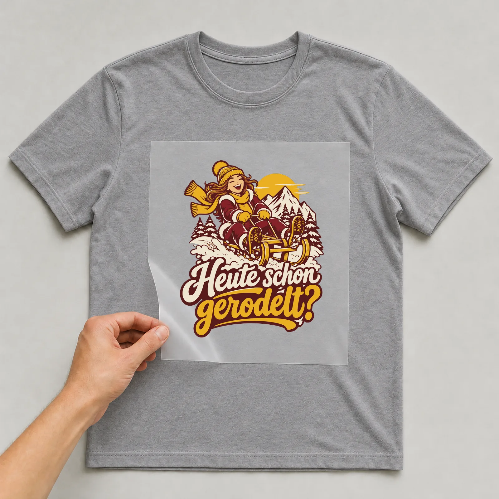 Bügelbild Heute schon gerodelt? auf grauem T-Shirt, Folie wird aufgelegt