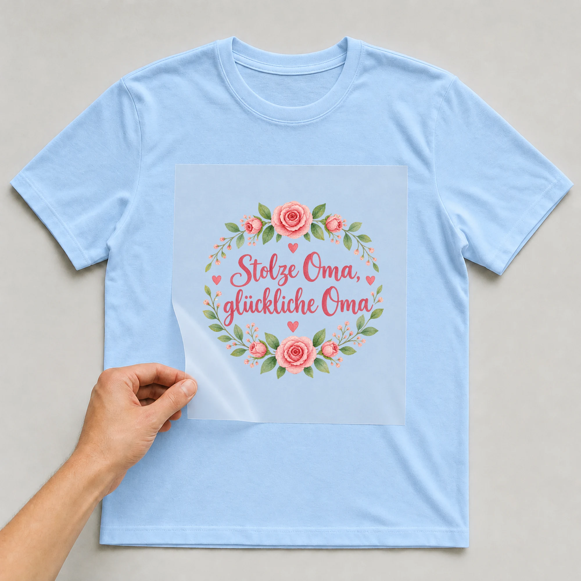 Bügelbild „Stolze Oma, glückliche Oma“ auf babyblauem T-Shirt, Folie wird aufgelegt