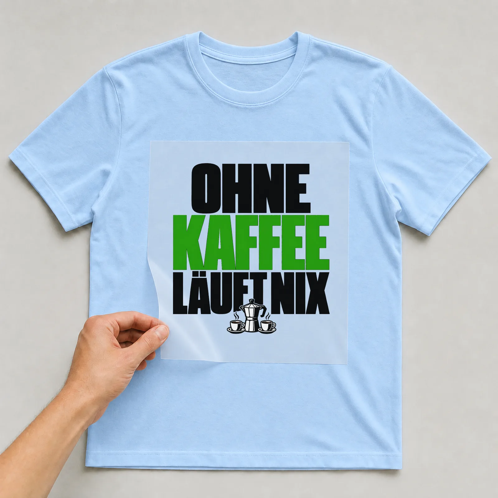 Bügelbild „Ohne Kaffee läuft nix“ auf hellblauem T-Shirt, Folie wird aufgelegt
