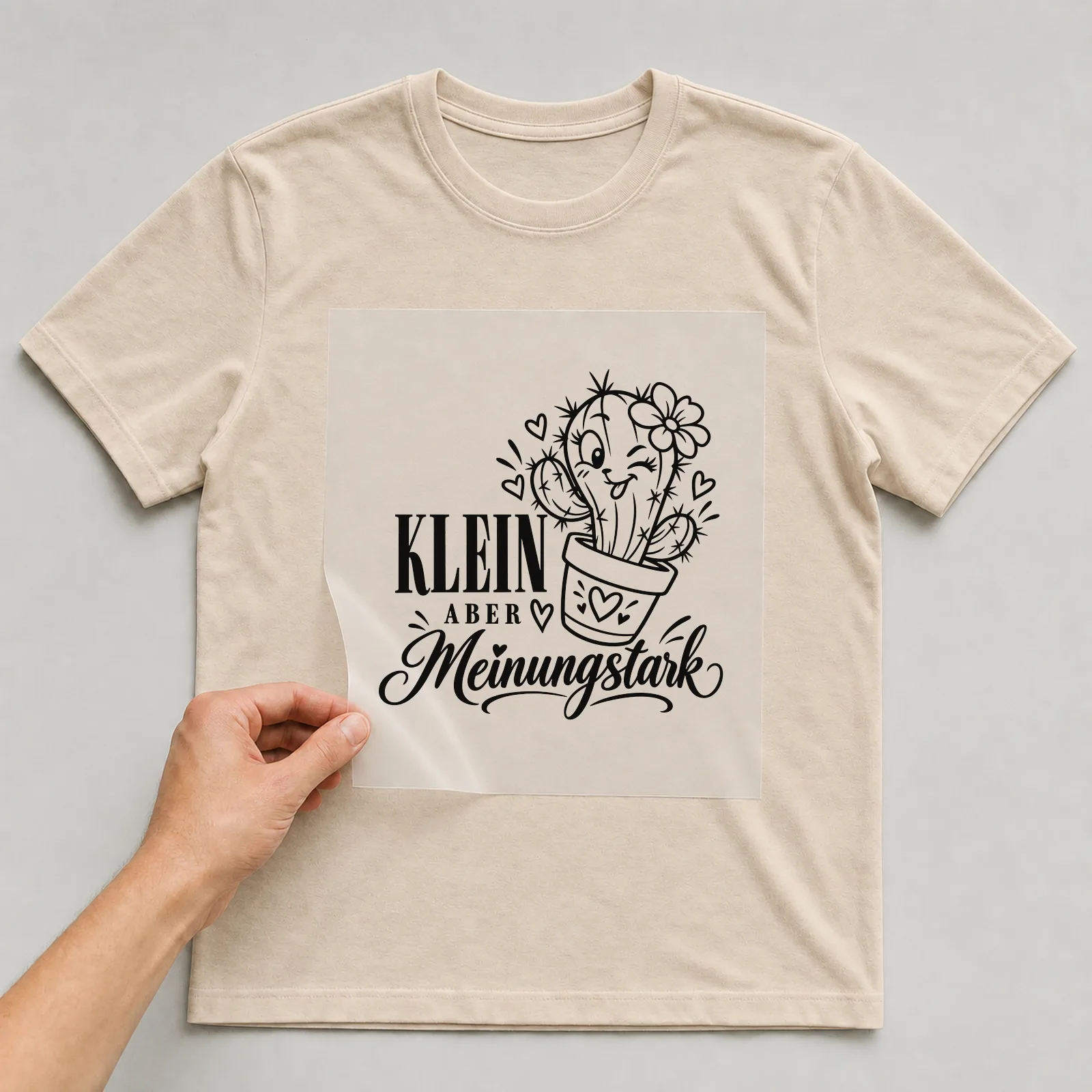 Bügelbild „Klein aber meinungsstark“ auf beigem T-Shirt, Folie wird aufgelegt