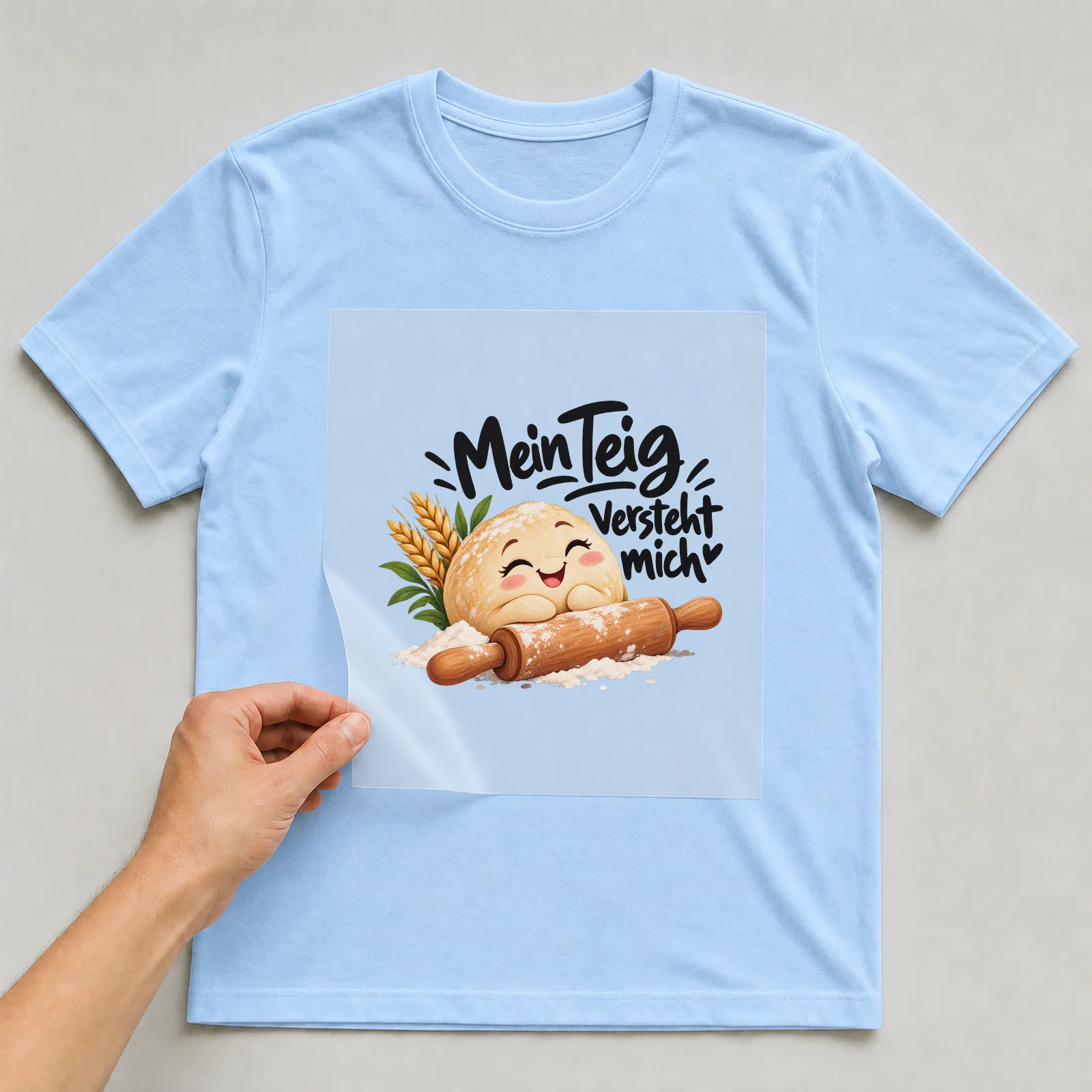 Bügelbild „Mein Teig versteht mich“ auf hellblauem T-Shirt, Folie wird aufgelegt