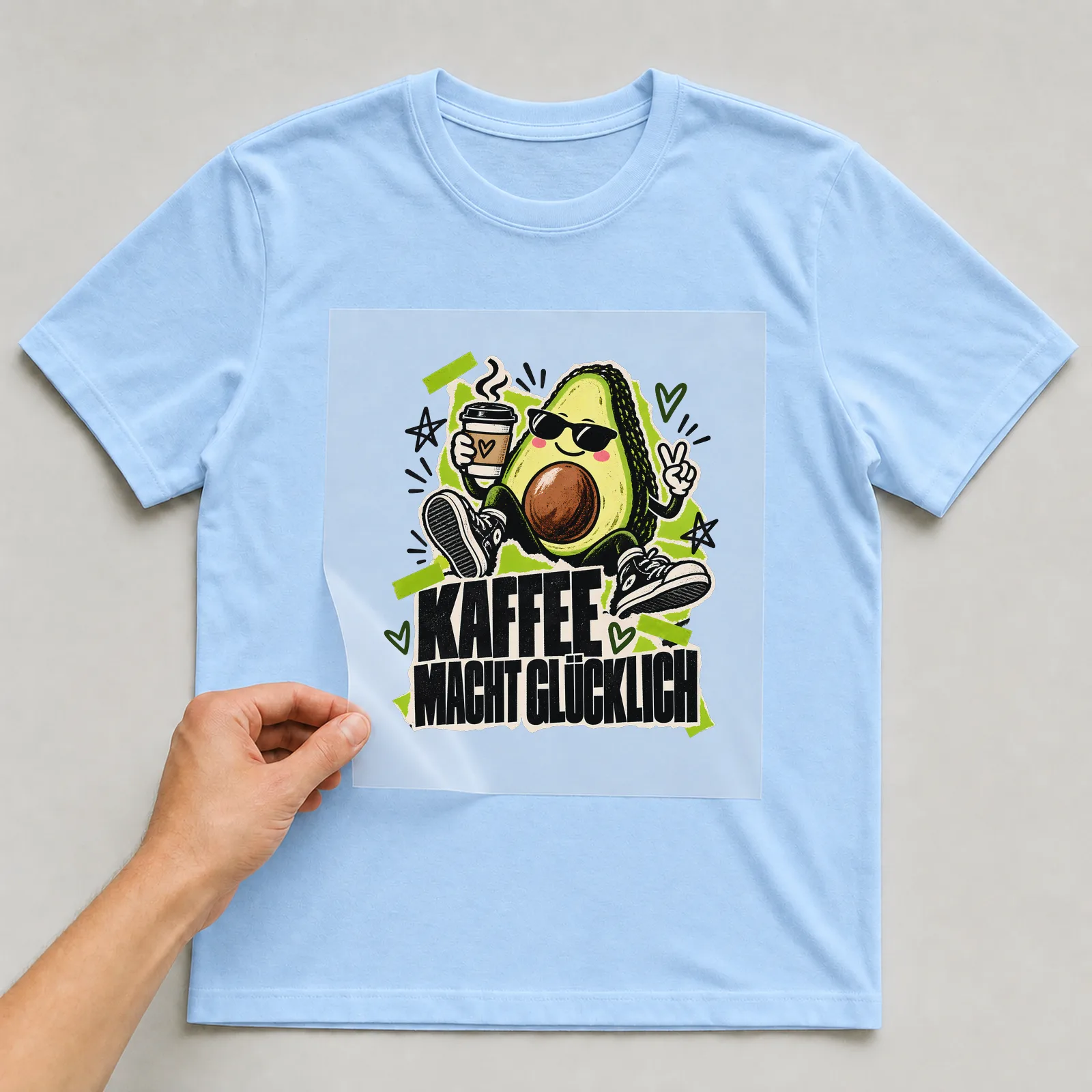Bügelbild „Kaffee macht glücklich“ (Zine-Collage-Stil) auf hellblauem T-Shirt, Folie wird aufgelegt
