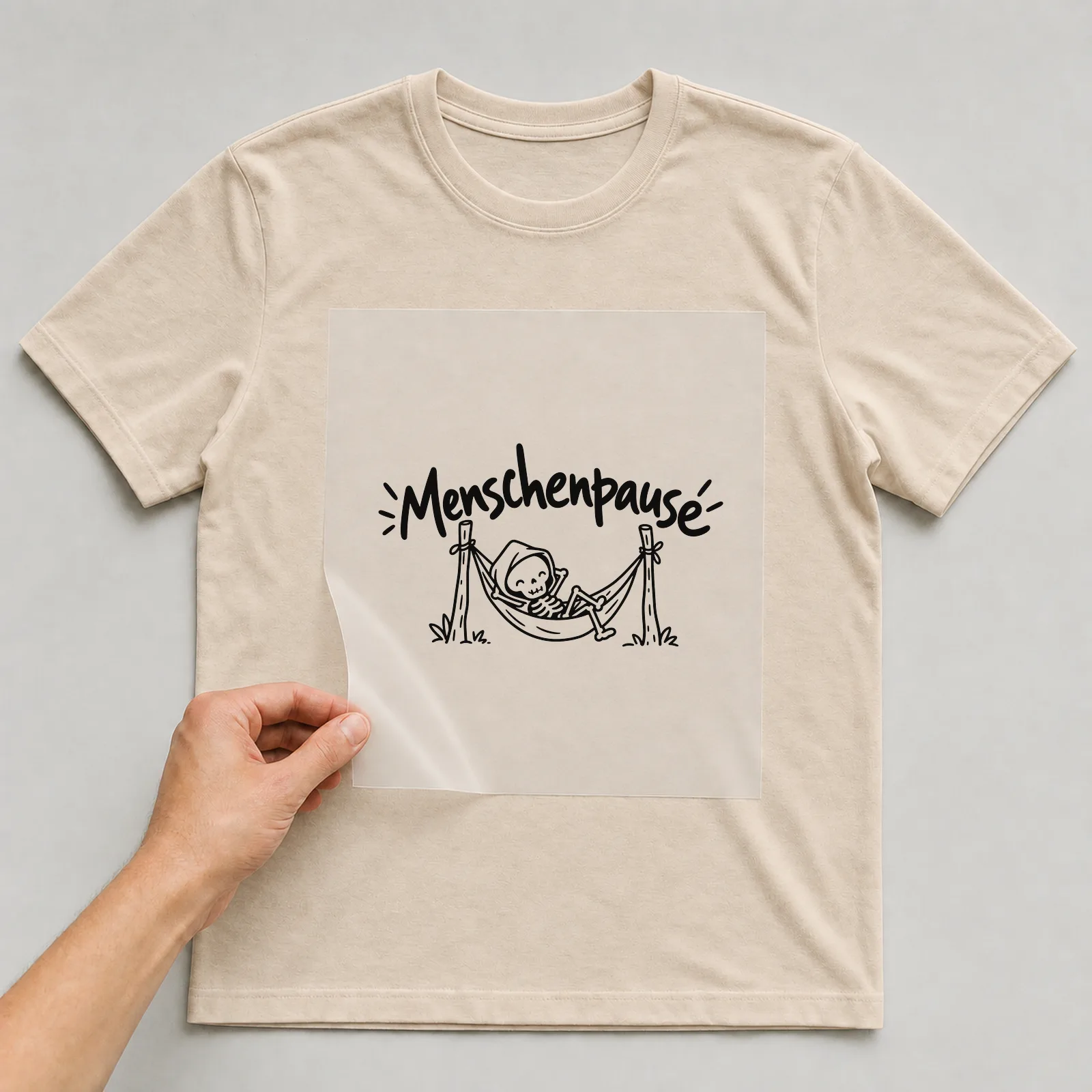 Bügelbild „Menschenpause“ auf beigem T-Shirt, Folie wird aufgelegt