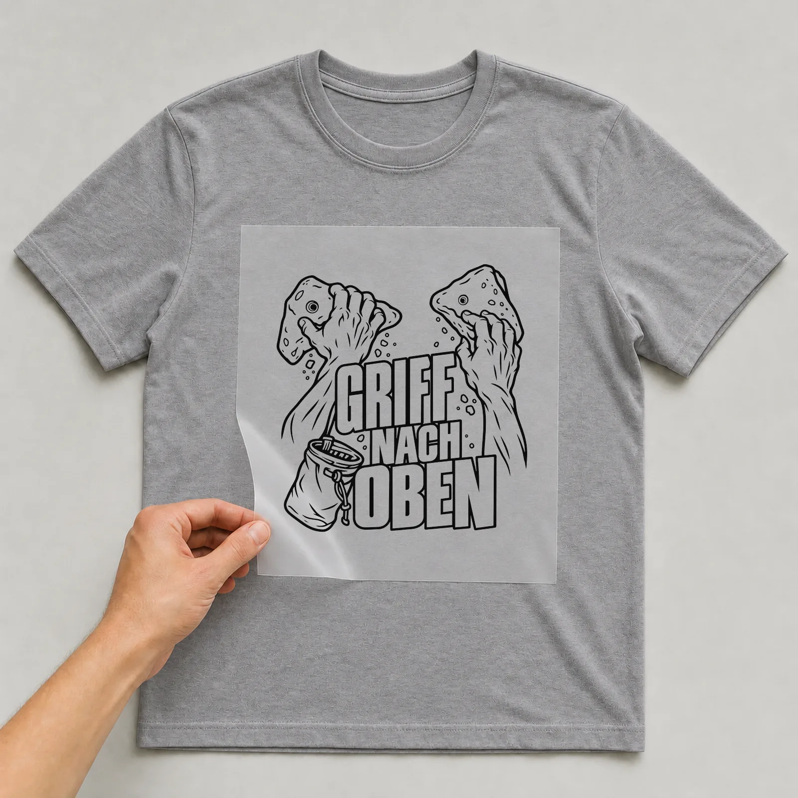 Bügelbild „Griff nach Oben“ auf grauem T-Shirt, Folie wird aufgelegt