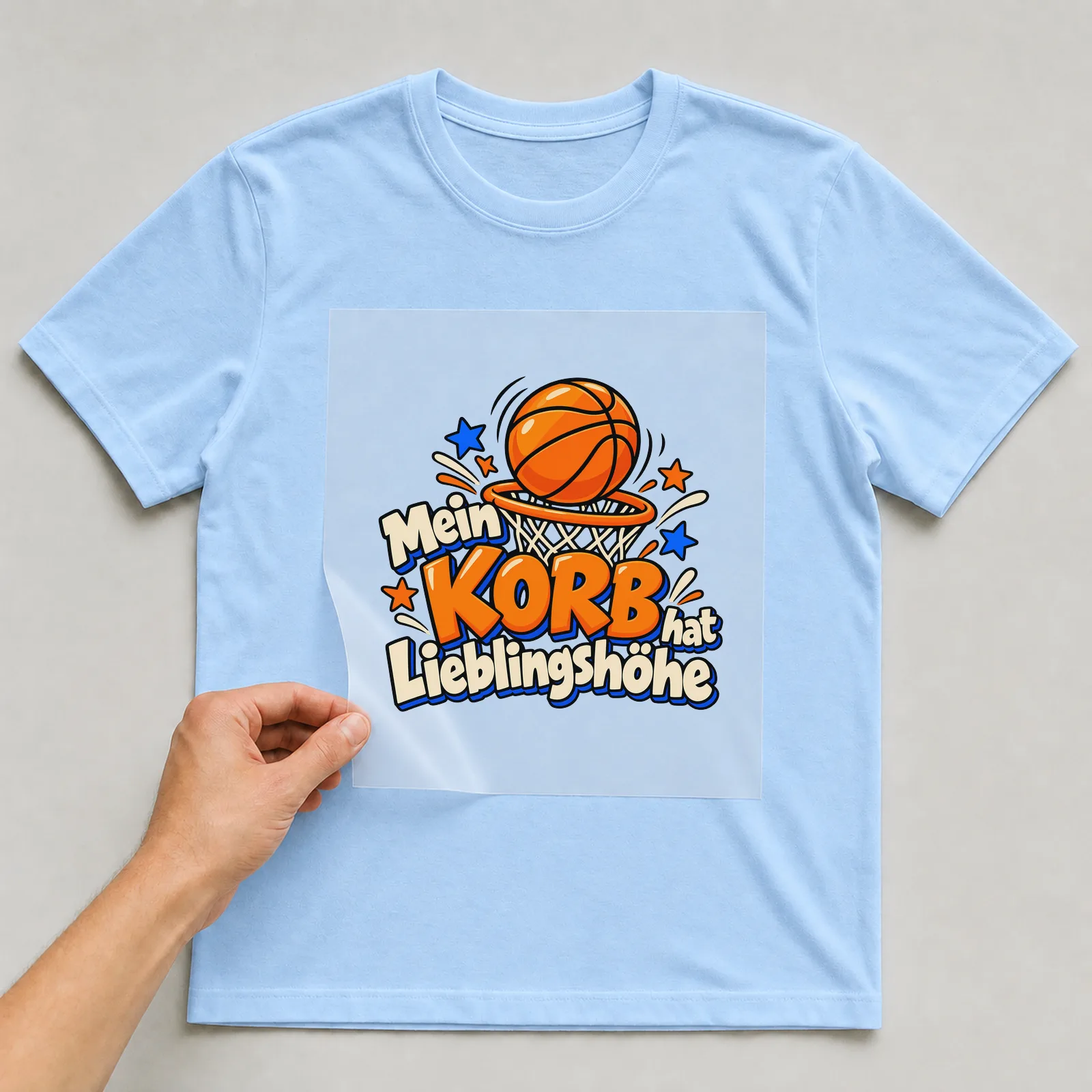 Bügelbild „Mein Korb hat Lieblingshöhe“ auf hellblauem T-Shirt, Folie wird aufgelegt