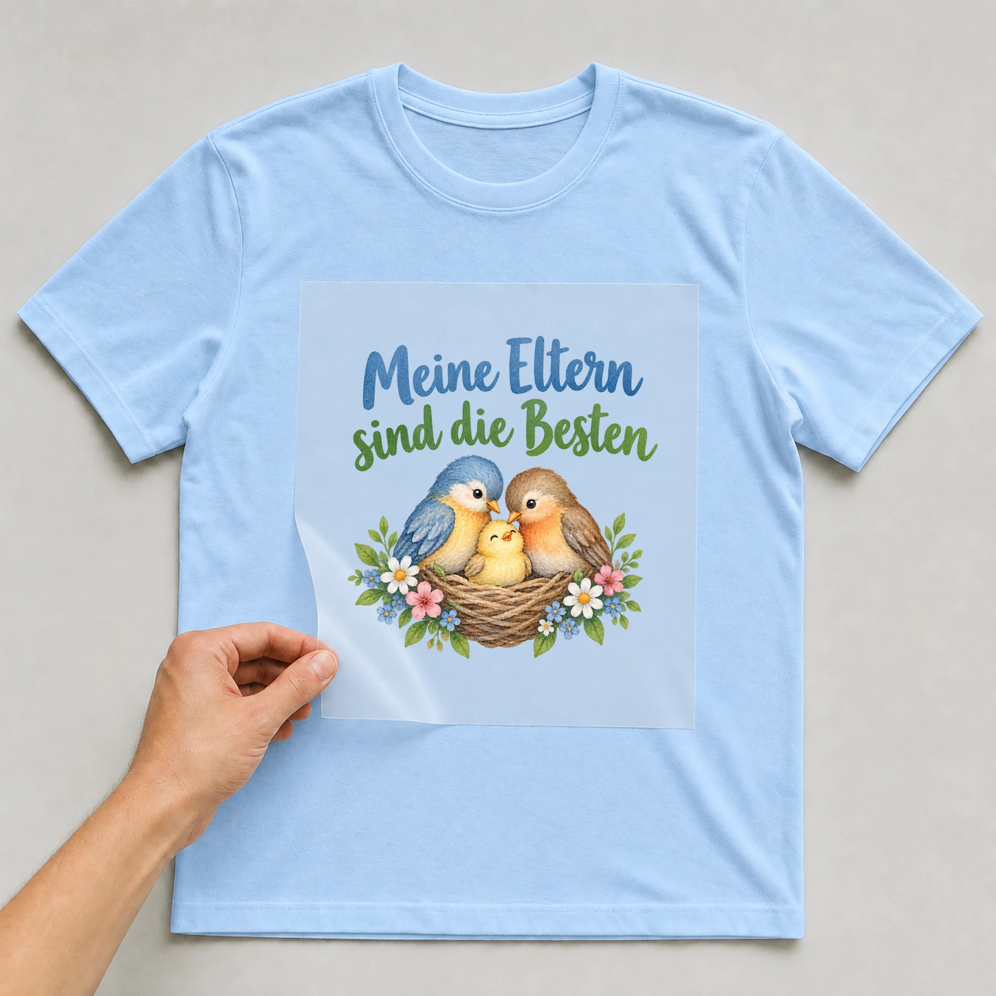 Bügelbild „Meine Eltern sind die Besten“ auf babyblauem T-Shirt, Folie wird aufgelegt