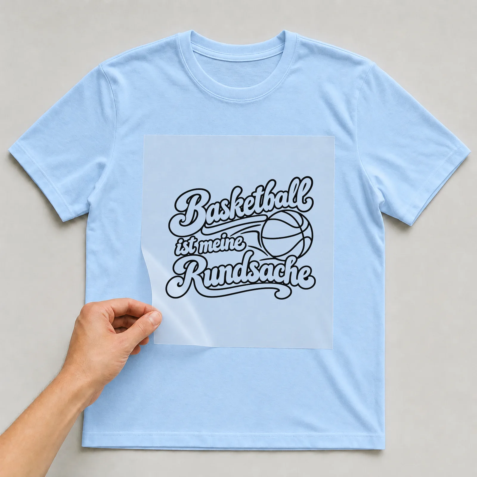 Bügelbild „Basketball ist meine Rundsache“ auf hellblauem T-Shirt, Folie wird aufgelegt