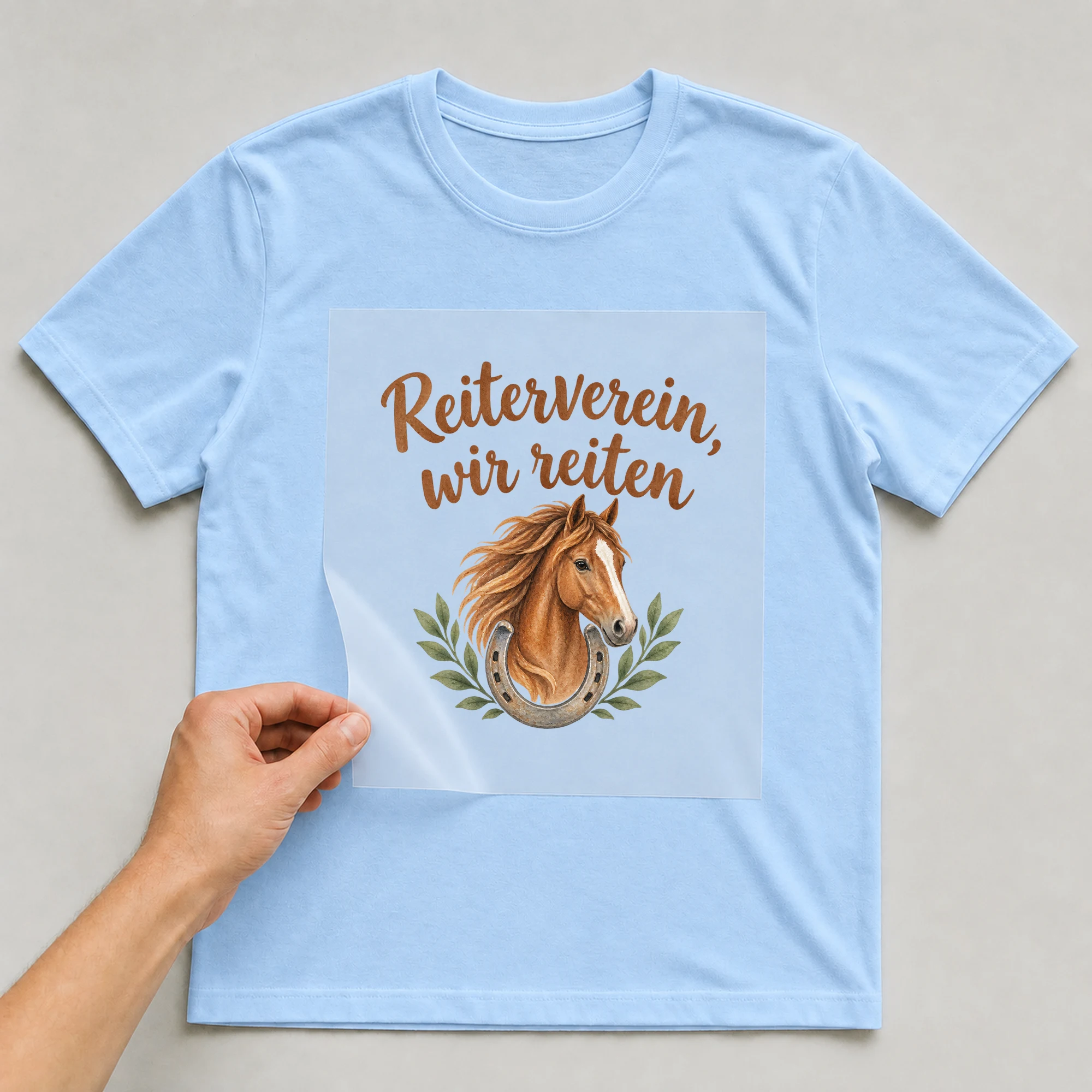 Bügelbild „Reiterverein, wir reiten“ auf babyblauem T-Shirt, Folie wird aufgelegt
