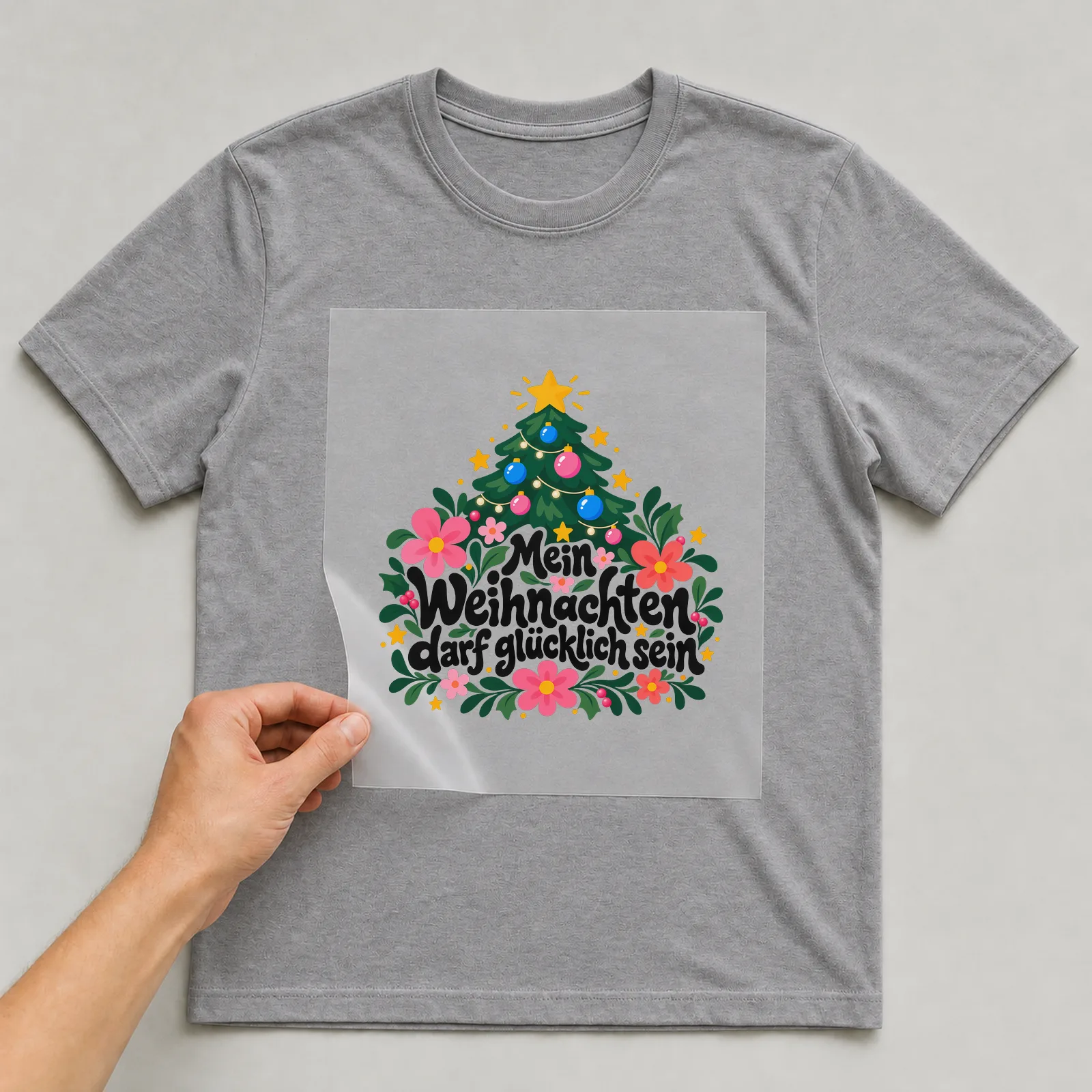 Bügelbild „Mein Weihnachten darf glücklich sein“ auf grauem T-Shirt, Folie wird aufgelegt